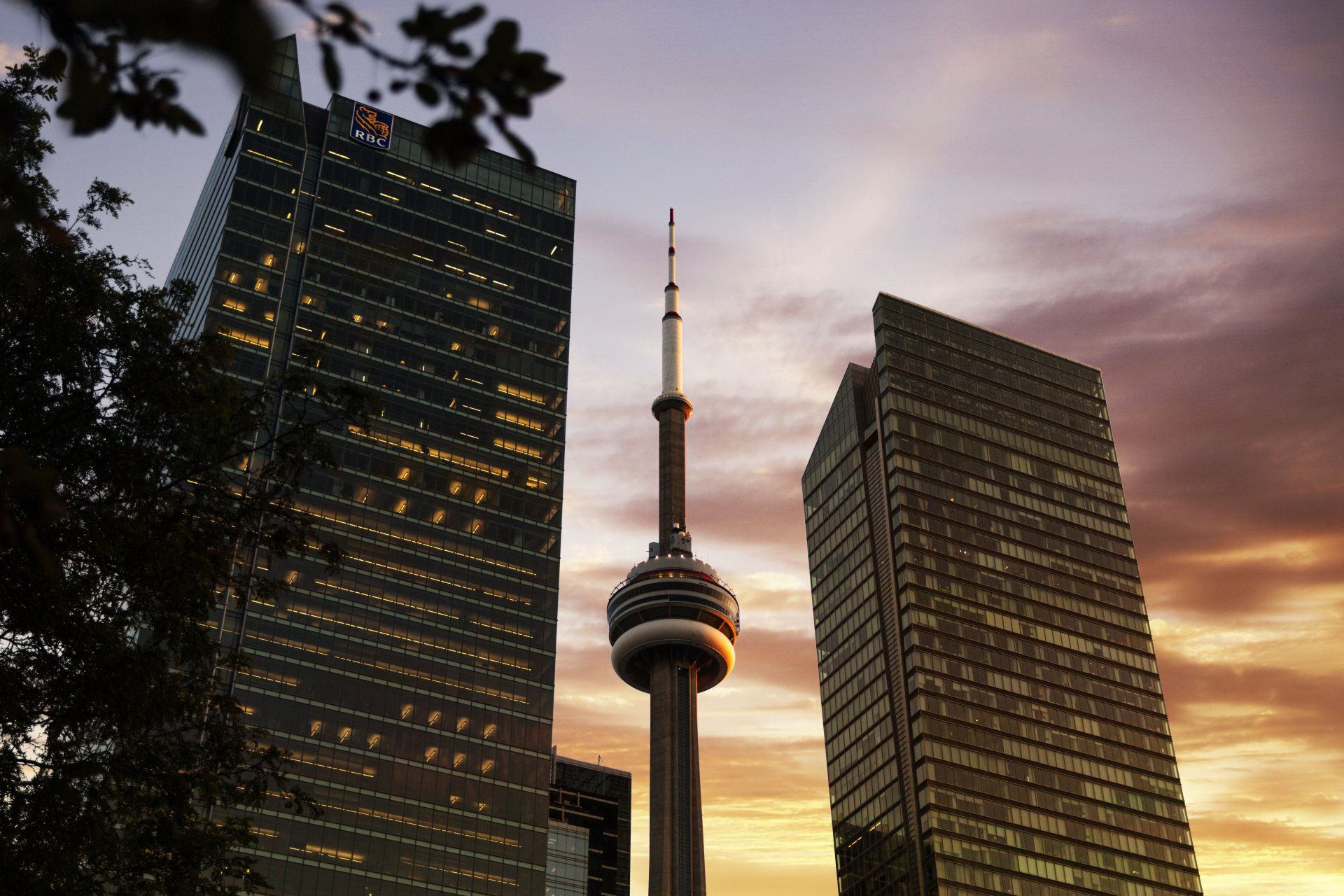 CN Tower in Toronto framed by tall buildings at sunset.