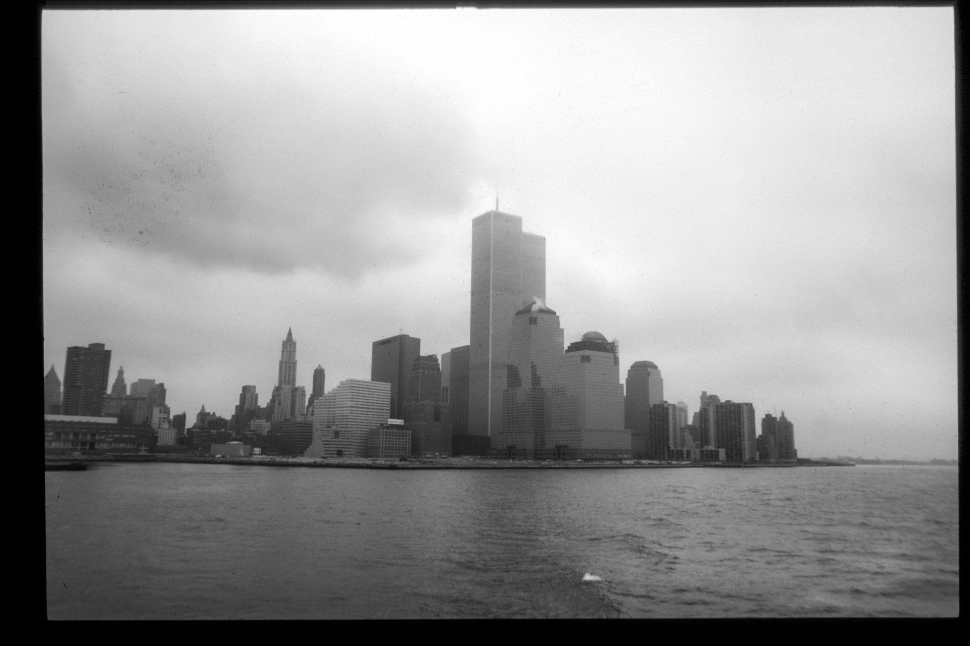A black and white photo of the New York City skyline with the Twin Towers visible, under a cloudy sky.