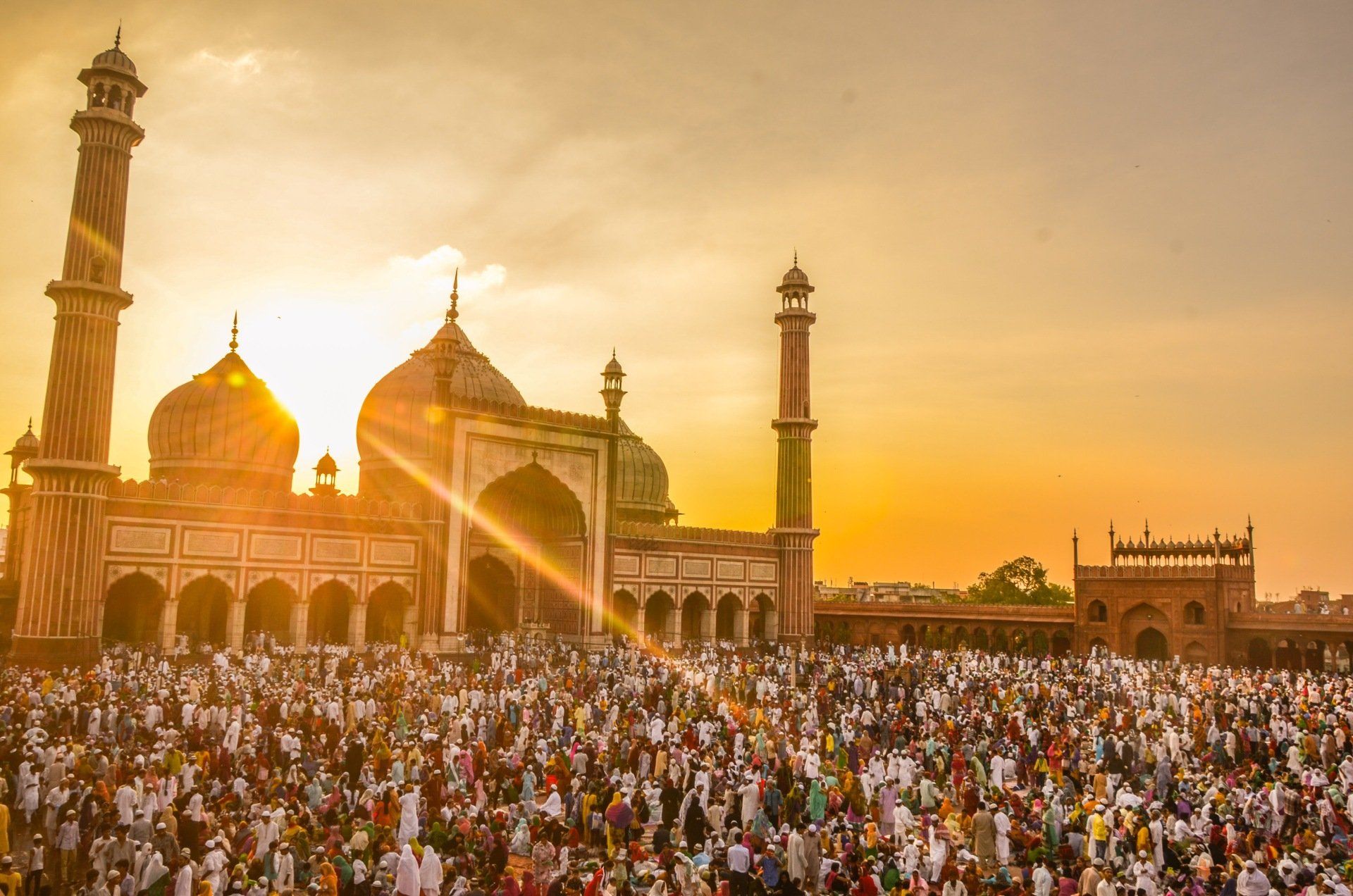 A large group of people are gathered in front of a mosque at sunset.