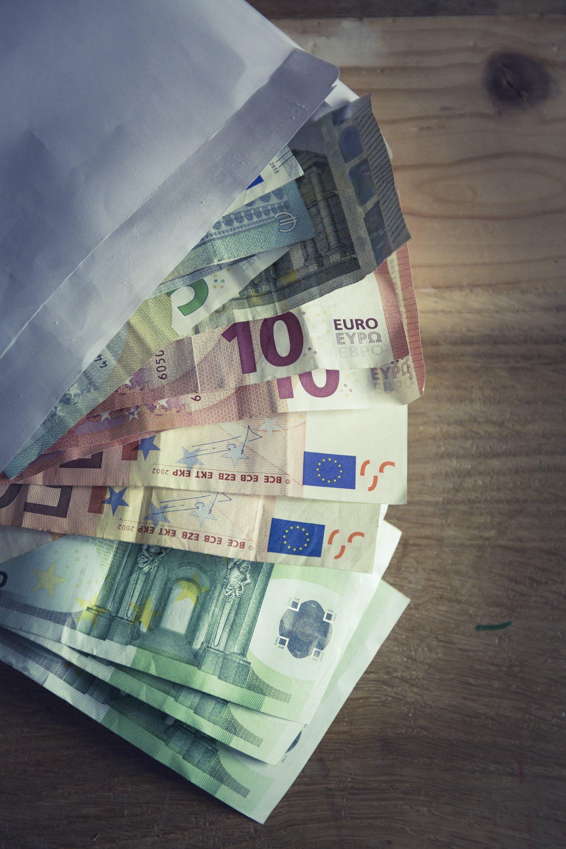 Een stapel eurobiljetten in een envelop op een houten tafel