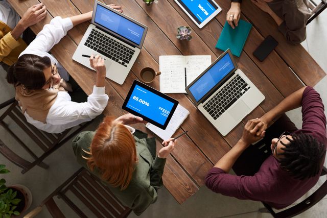 A group of people are sitting around a table with laptops and tablets.