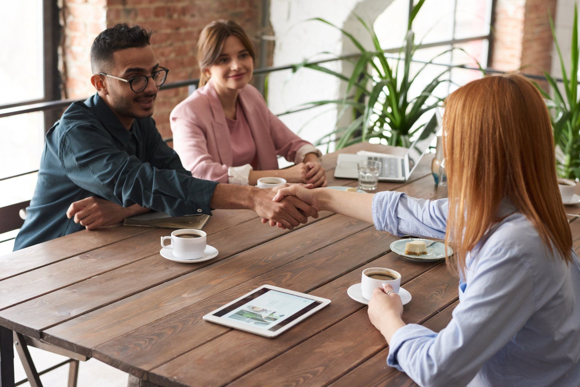 A woman is shaking hands with a man and a woman while sitting at a table.