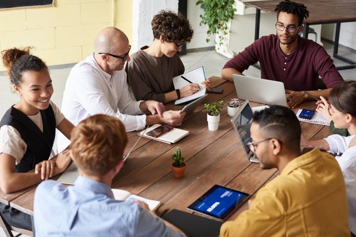 A group of people are sitting around a table with laptops and tablets.