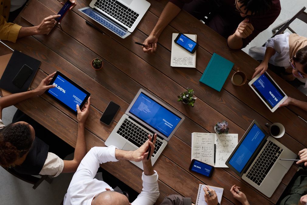 A group of people are sitting around a table with laptops and tablets.