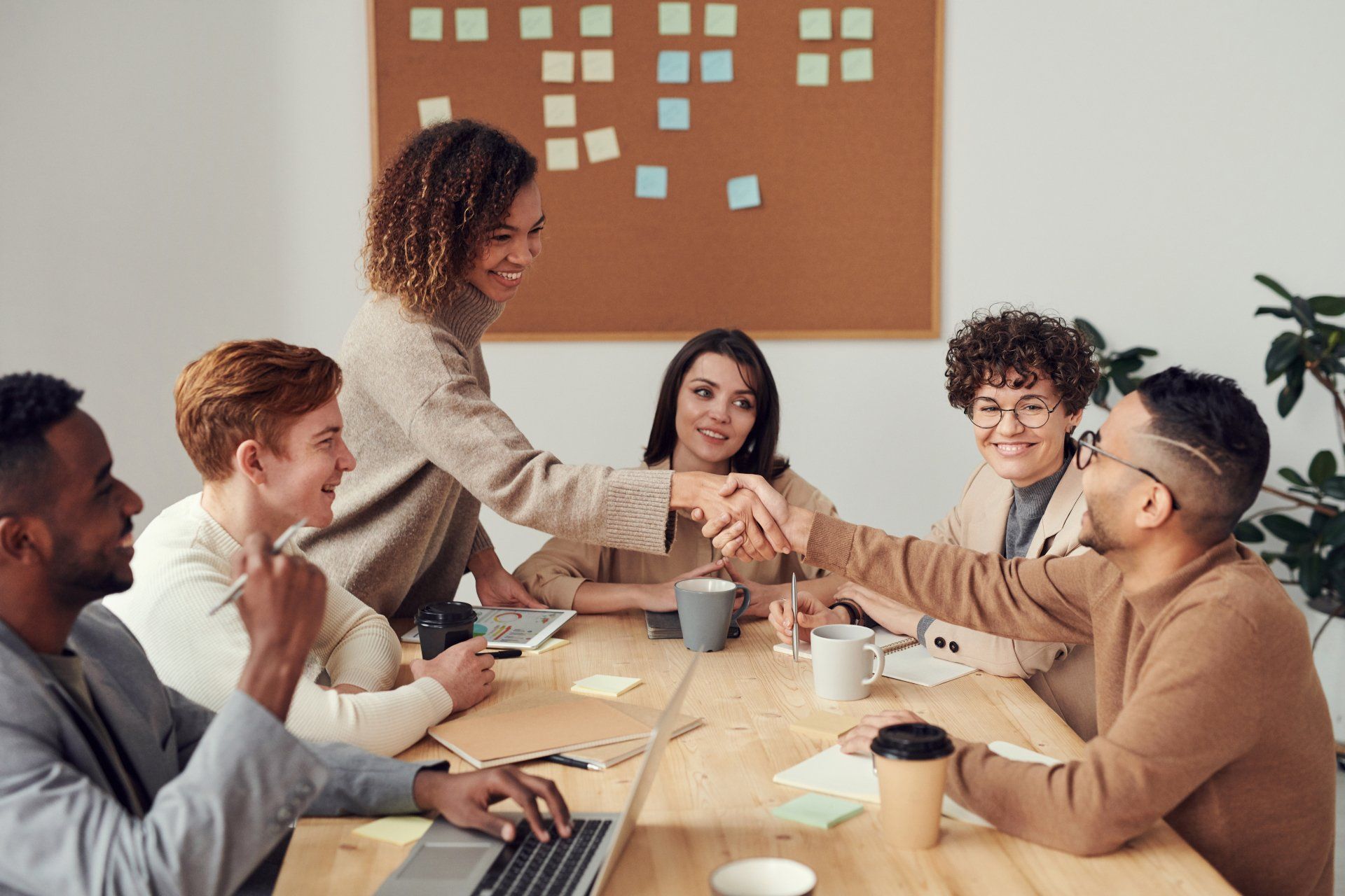 six people around a table with one standing, shaking another hand 