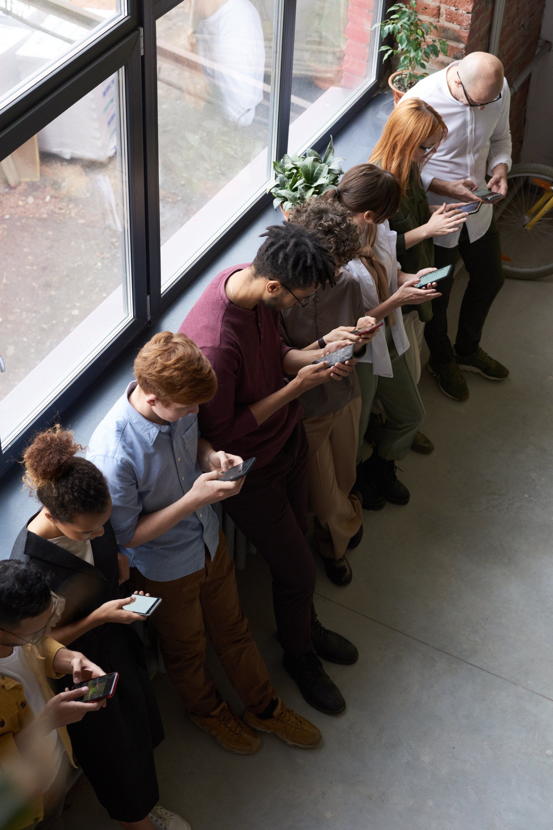 A group of people are standing in a line looking at their phones.