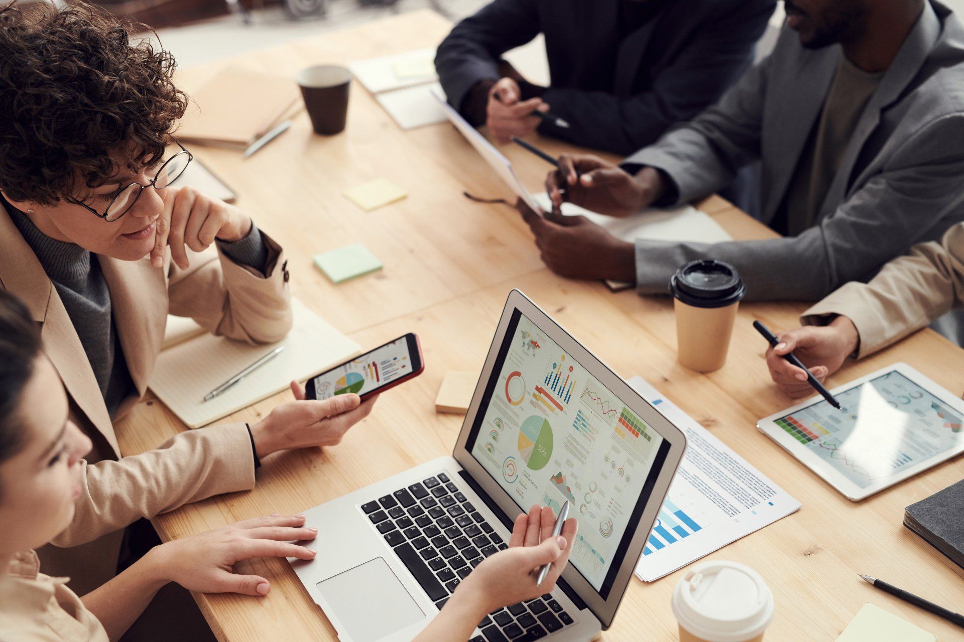 A group of people are sitting around a table with laptops and tablets.