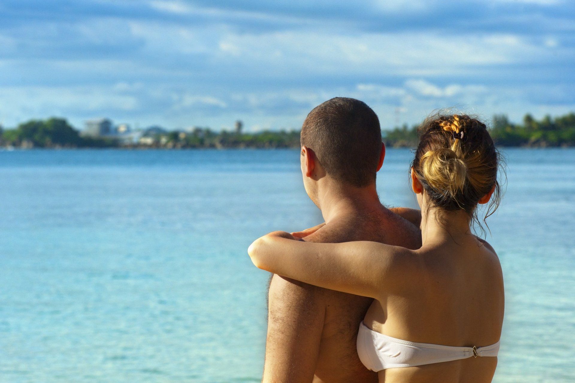 A man and a woman are standing on a beach looking at the ocean.