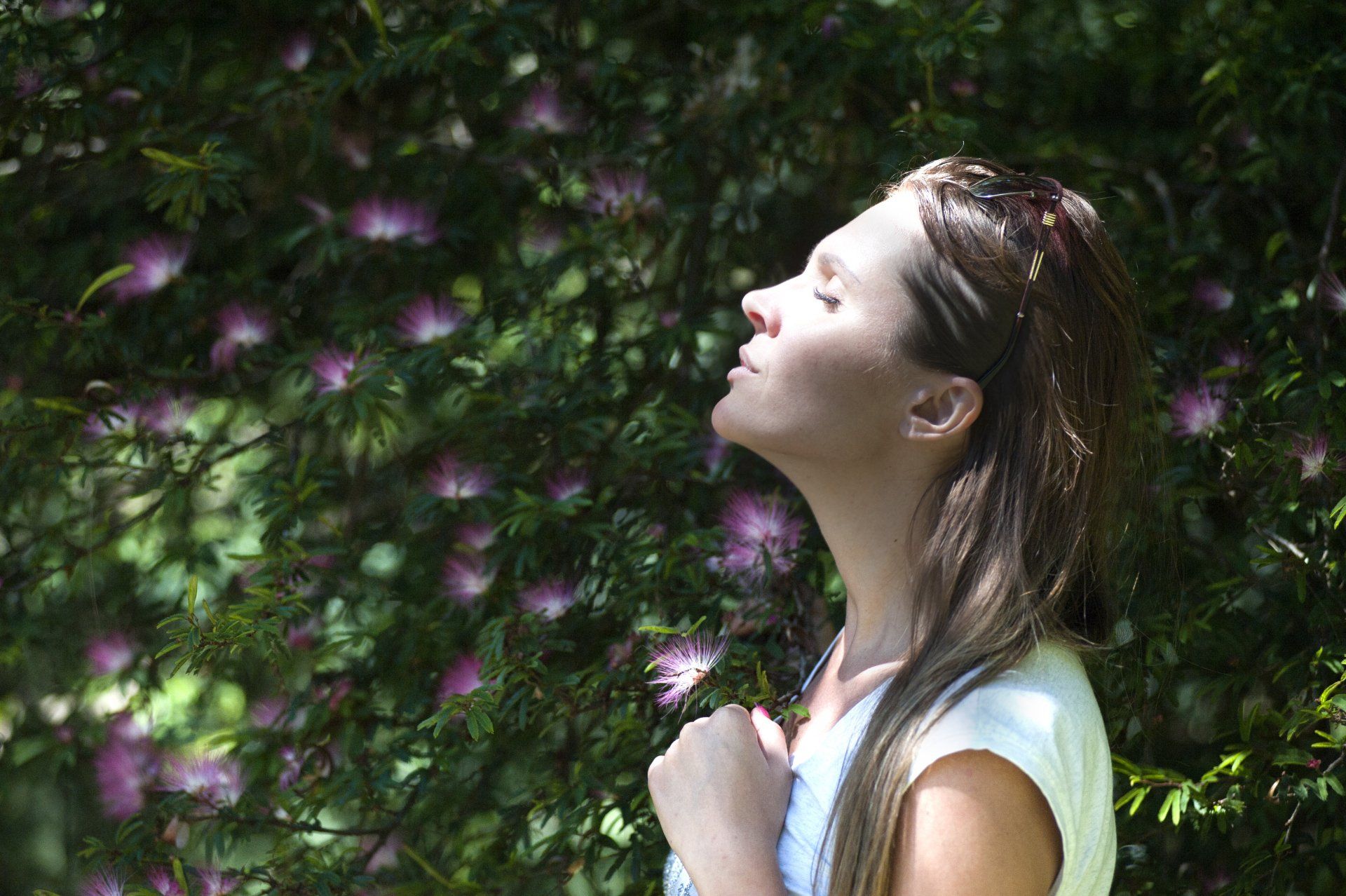 woman beside flowering shrub, lifting her face up to the sun