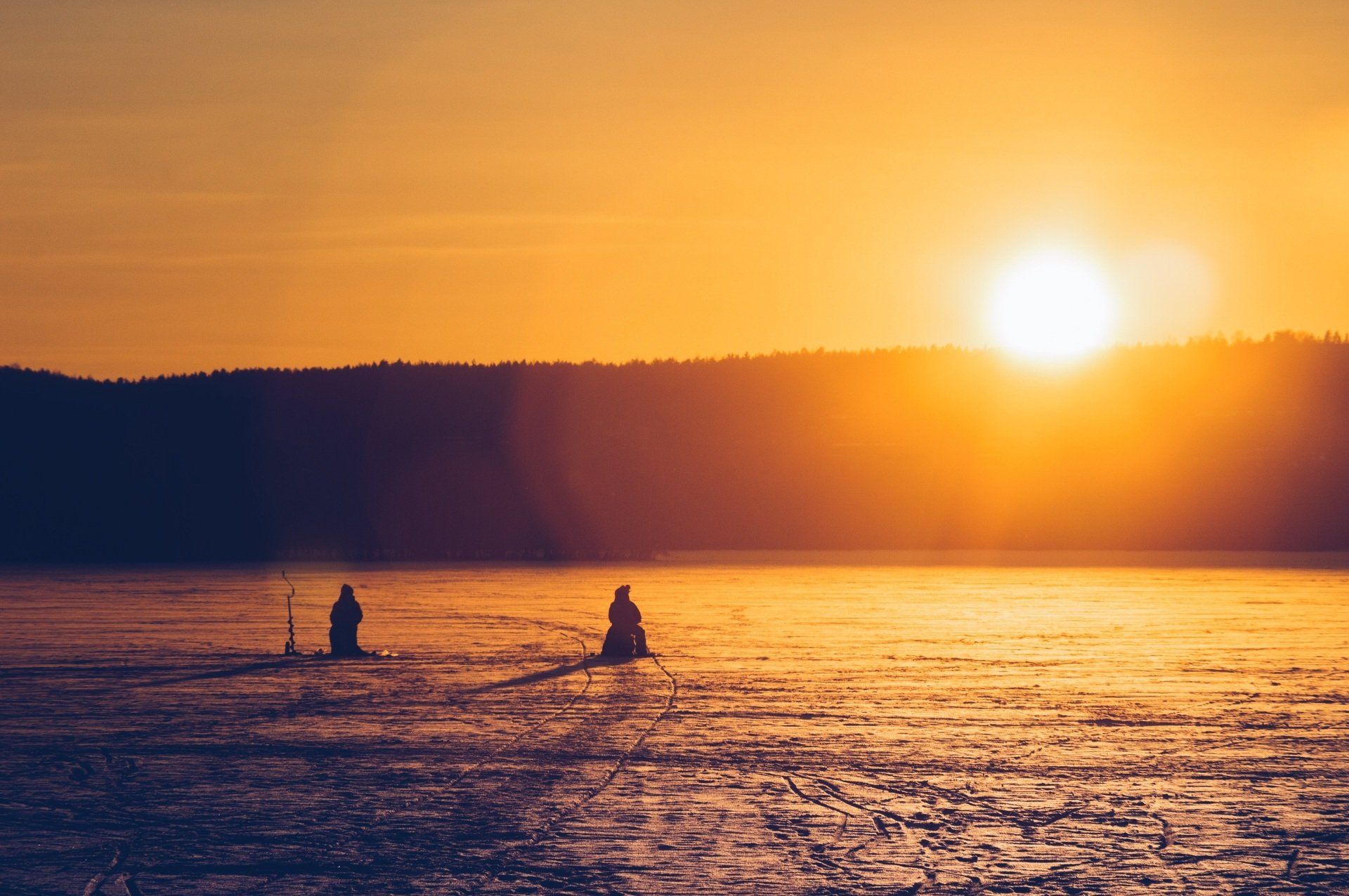 Two people are fishing in a lake at sunset.