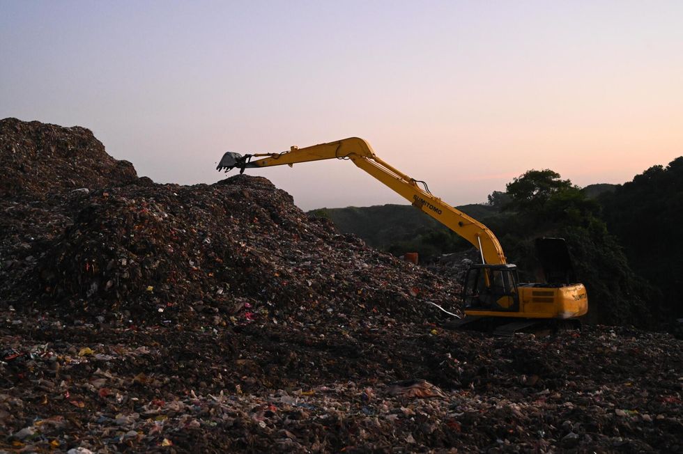 Yellow excavator on a mountain of garbage at dusk.