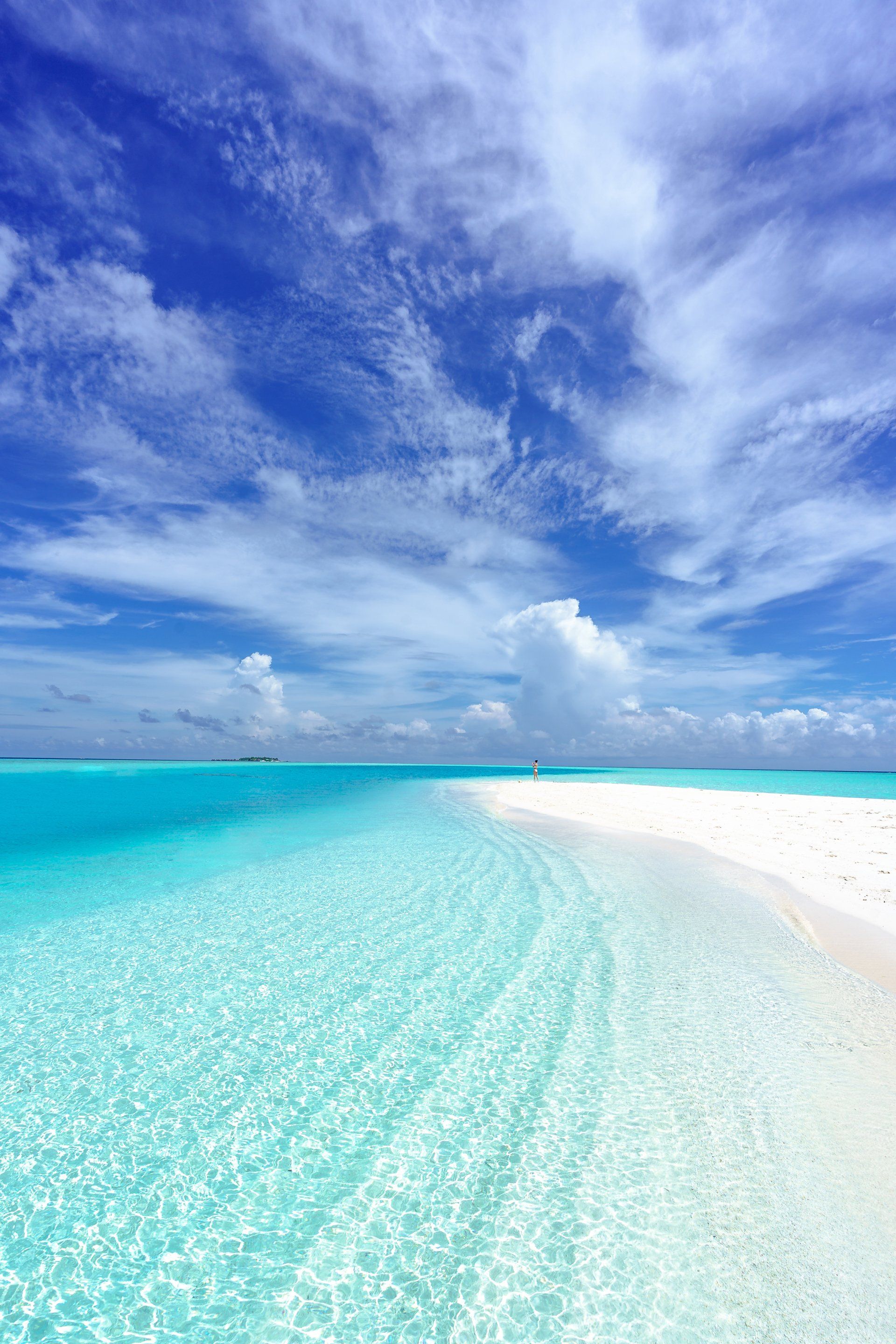 Türkisfarbenes Meerwasser trifft auf weißen Sandstrand unter einem strahlend blauen Himmel mit flauschigen Wolken.