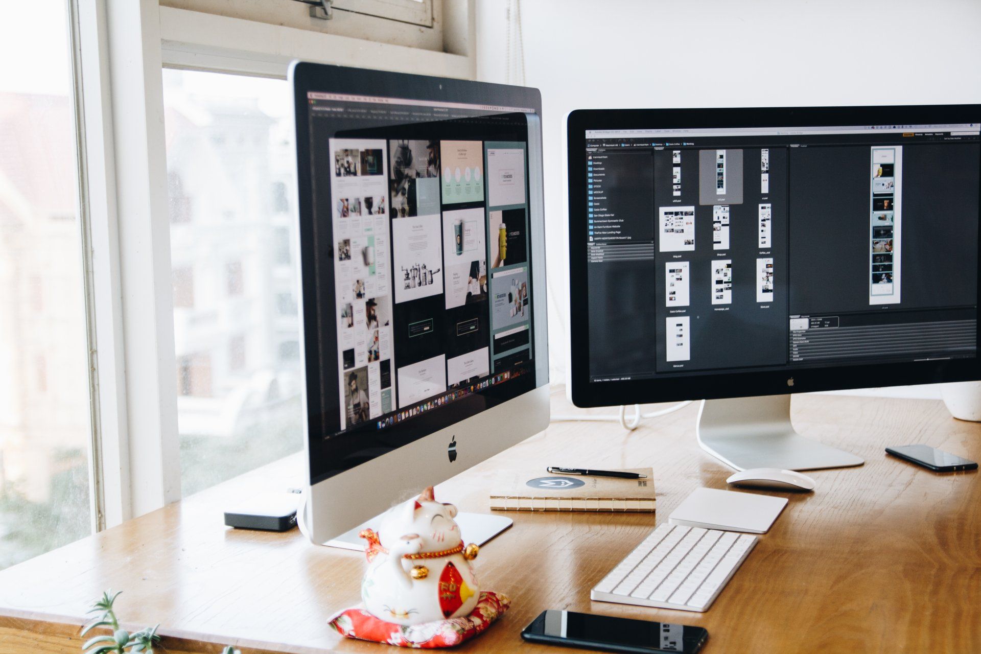 Two computer monitors are sitting on a wooden desk next to a window.