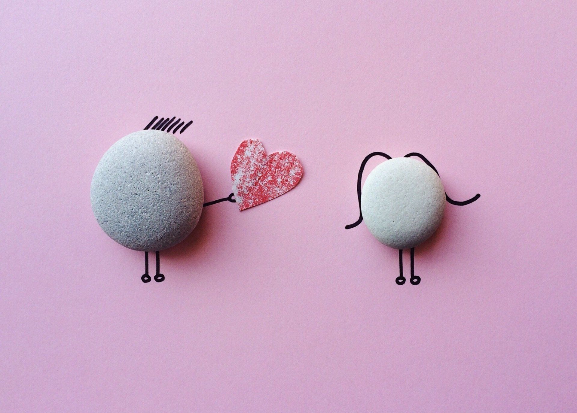 two rocks with arms and legs and a heart on a pink background .