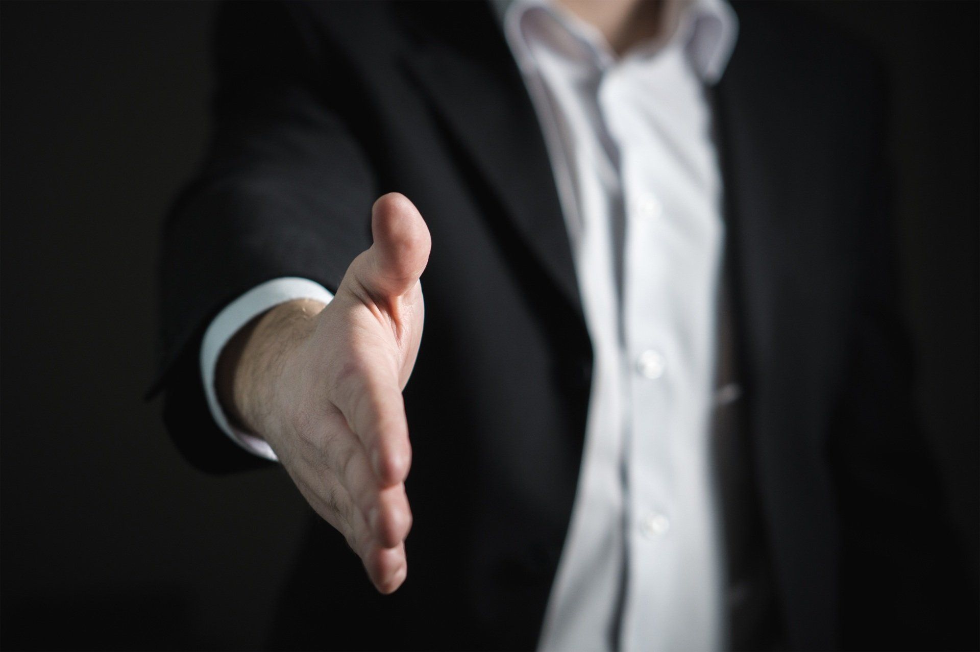 A man in a suit and white shirt is reaching out to shake someone 's hand.