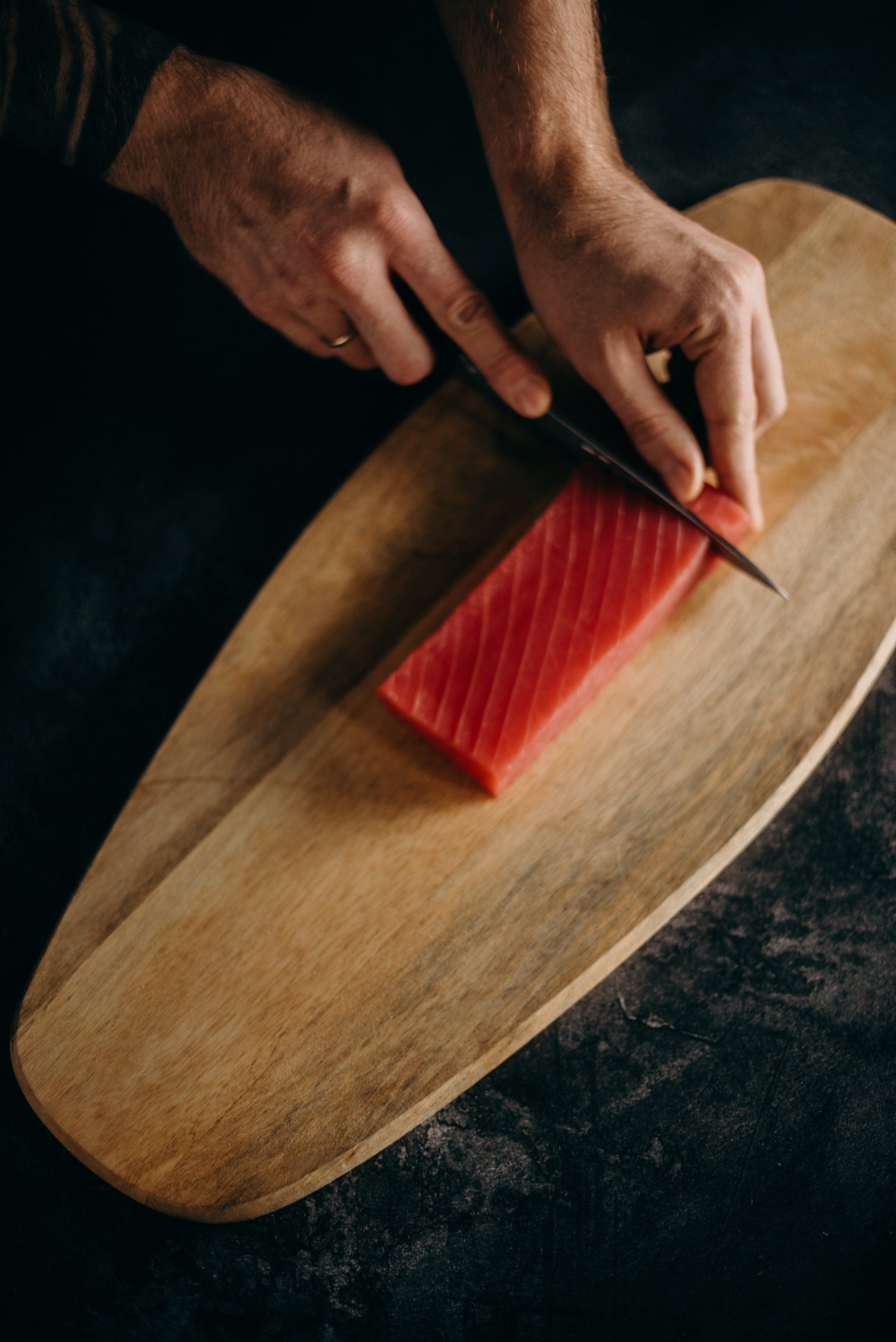 A person is cutting a piece of meat on a wooden cutting board.