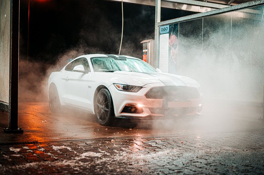 A white ford mustang is being washed in a car wash.