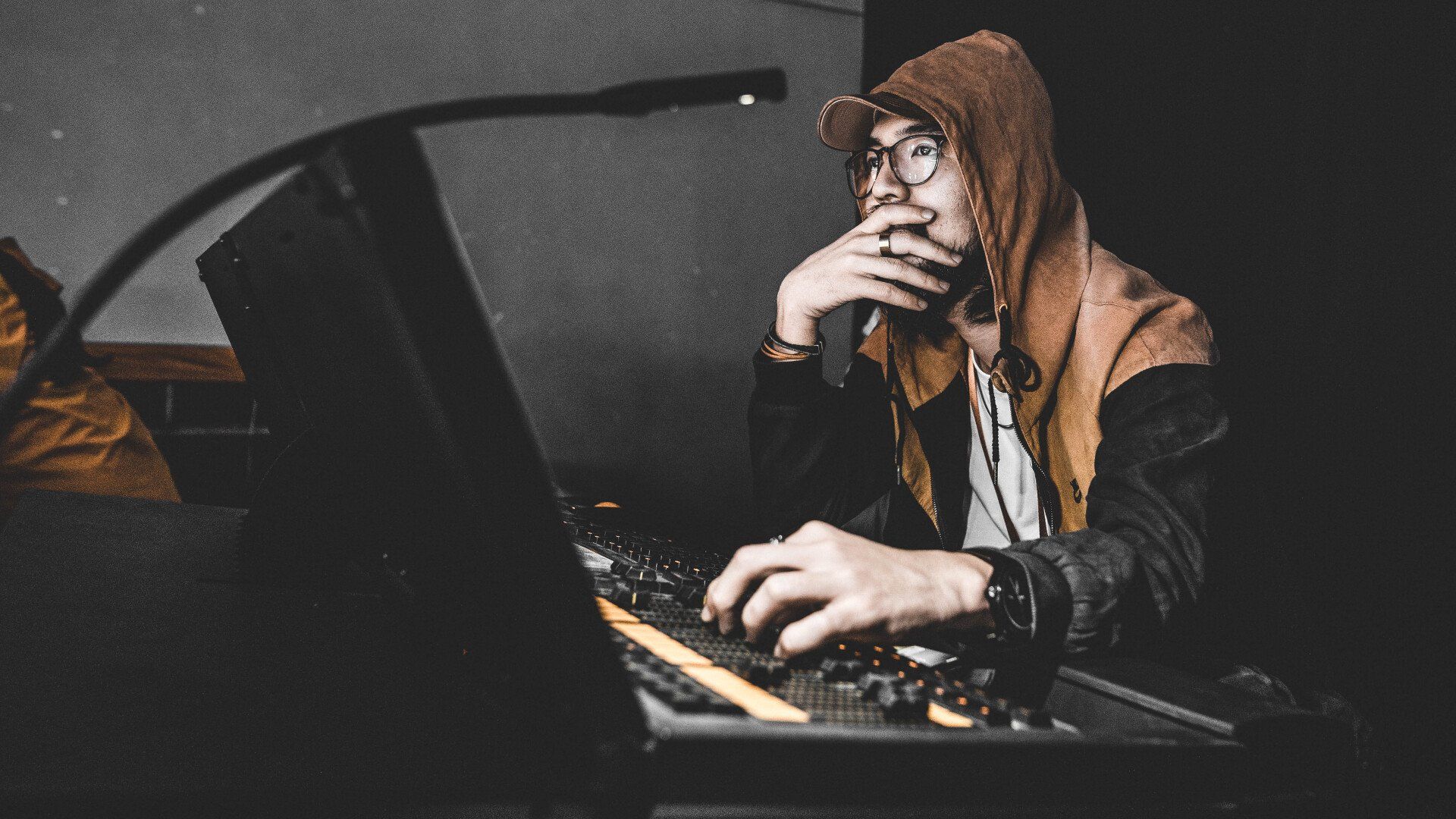 A man in a hoodie is sitting in a music production studio.