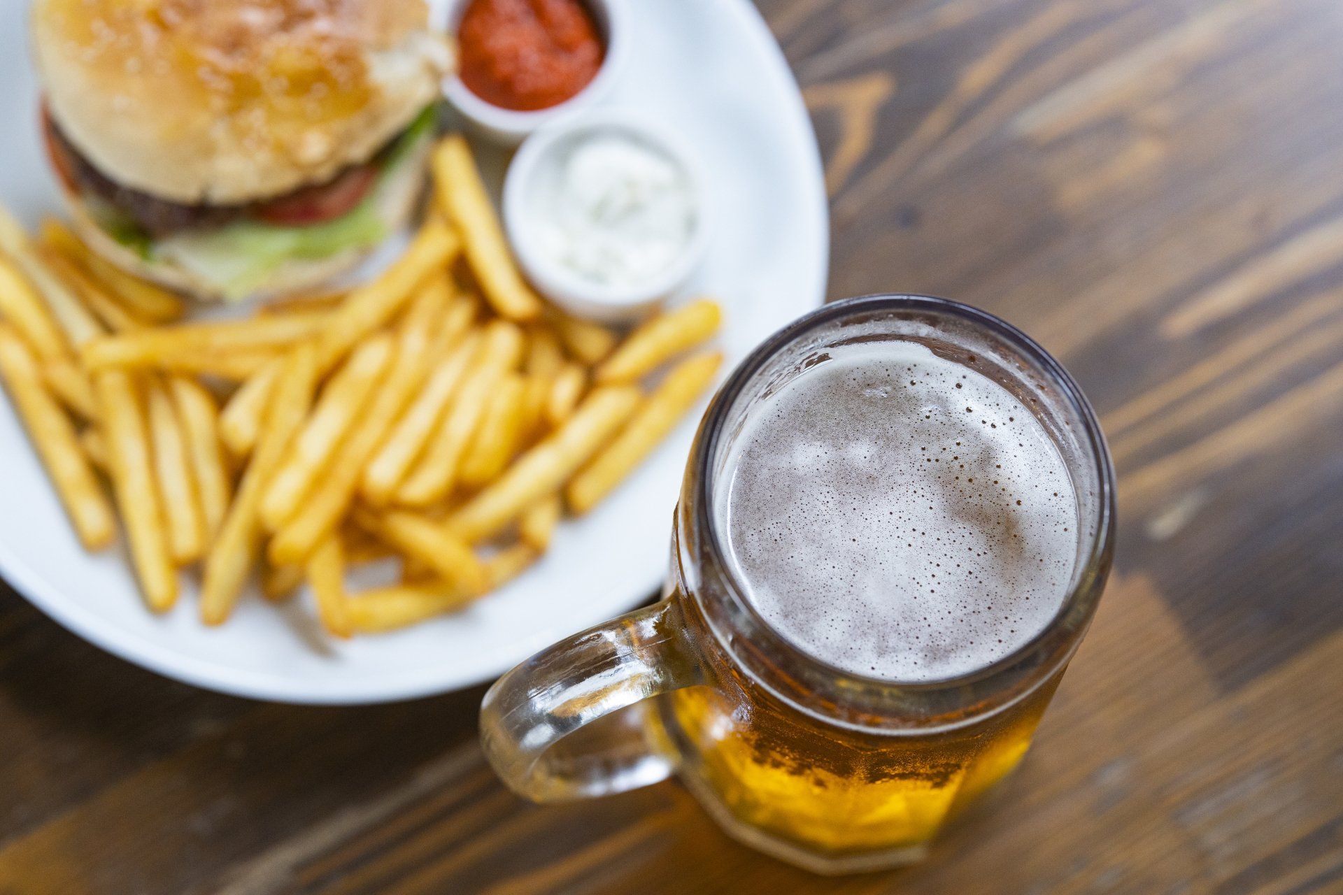 a plate of french fries and a hamburger next to a glass of beer on a wooden table .