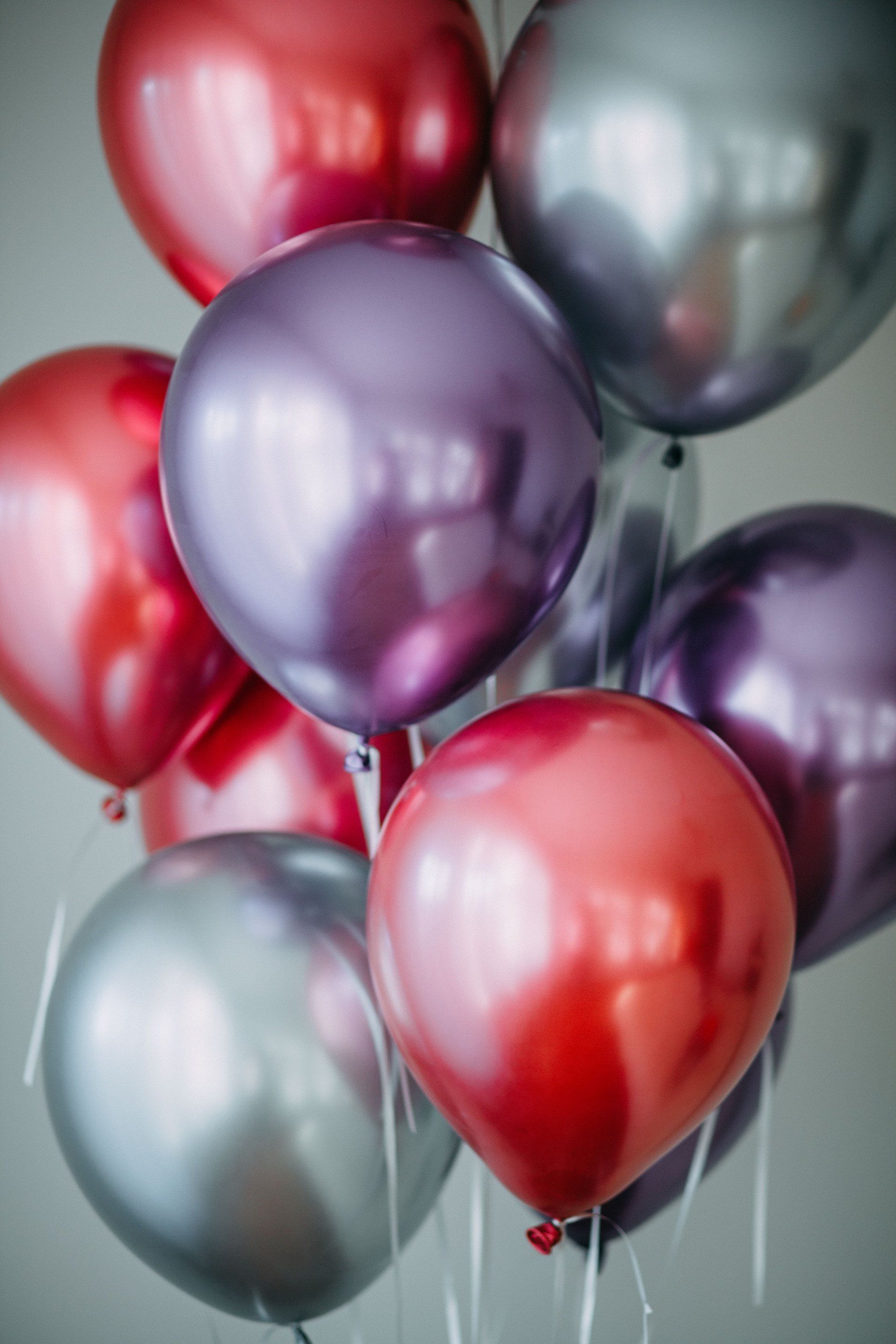 A bunch of red , purple and silver balloons hanging from a string.