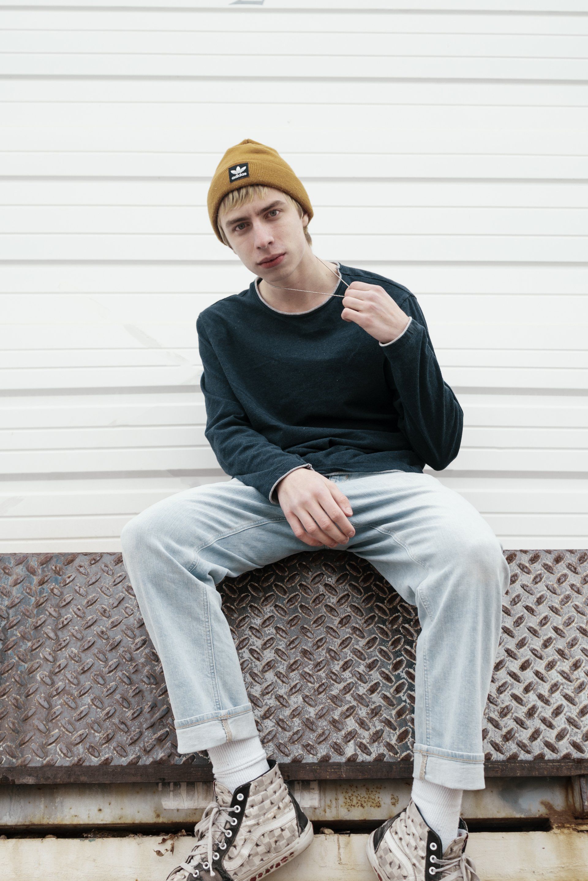 A young man wearing a beanie and jeans is sitting on a metal block.