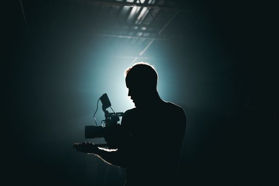 backlit silhouette of a filmmaker setting up his next shot with his camera in hand