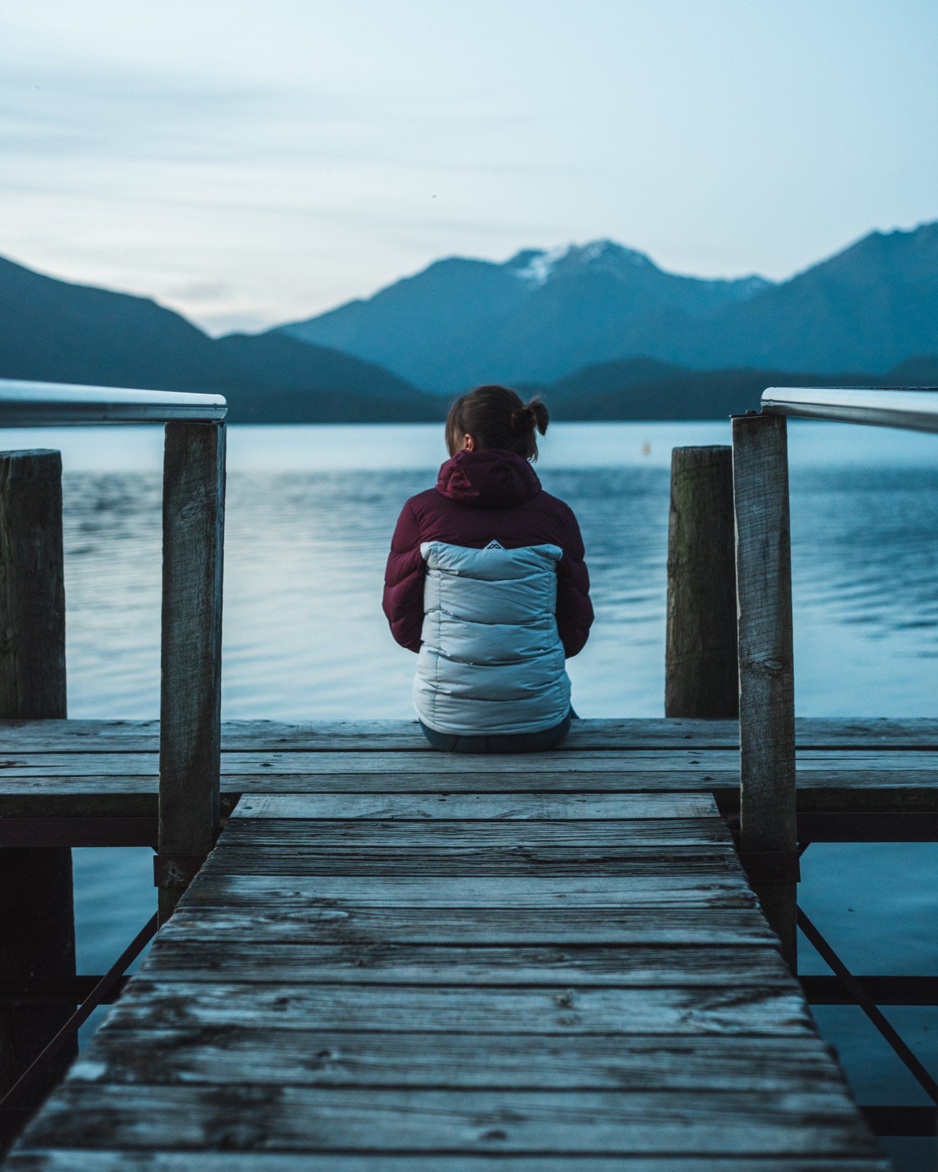 A woman is sitting on a wooden dock overlooking a lake.