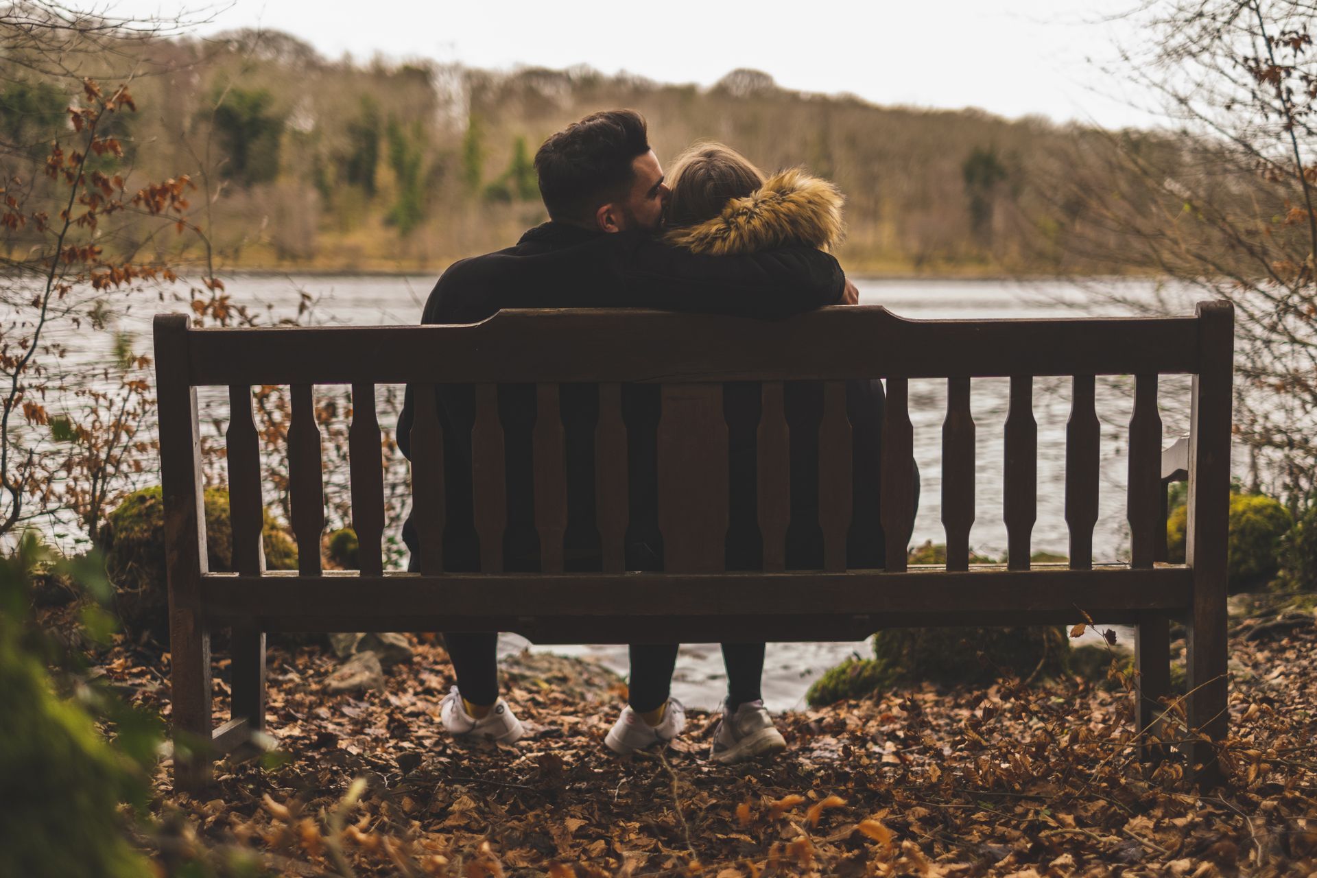 A man and a woman are sitting on a bench near a lake.