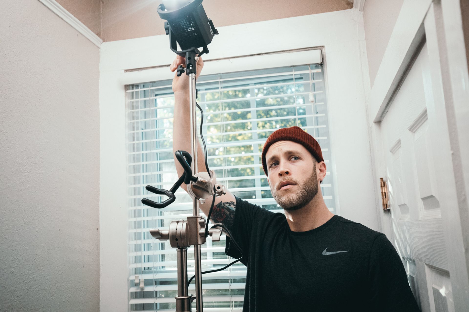 A man is holding a camera on a tripod in front of a window.