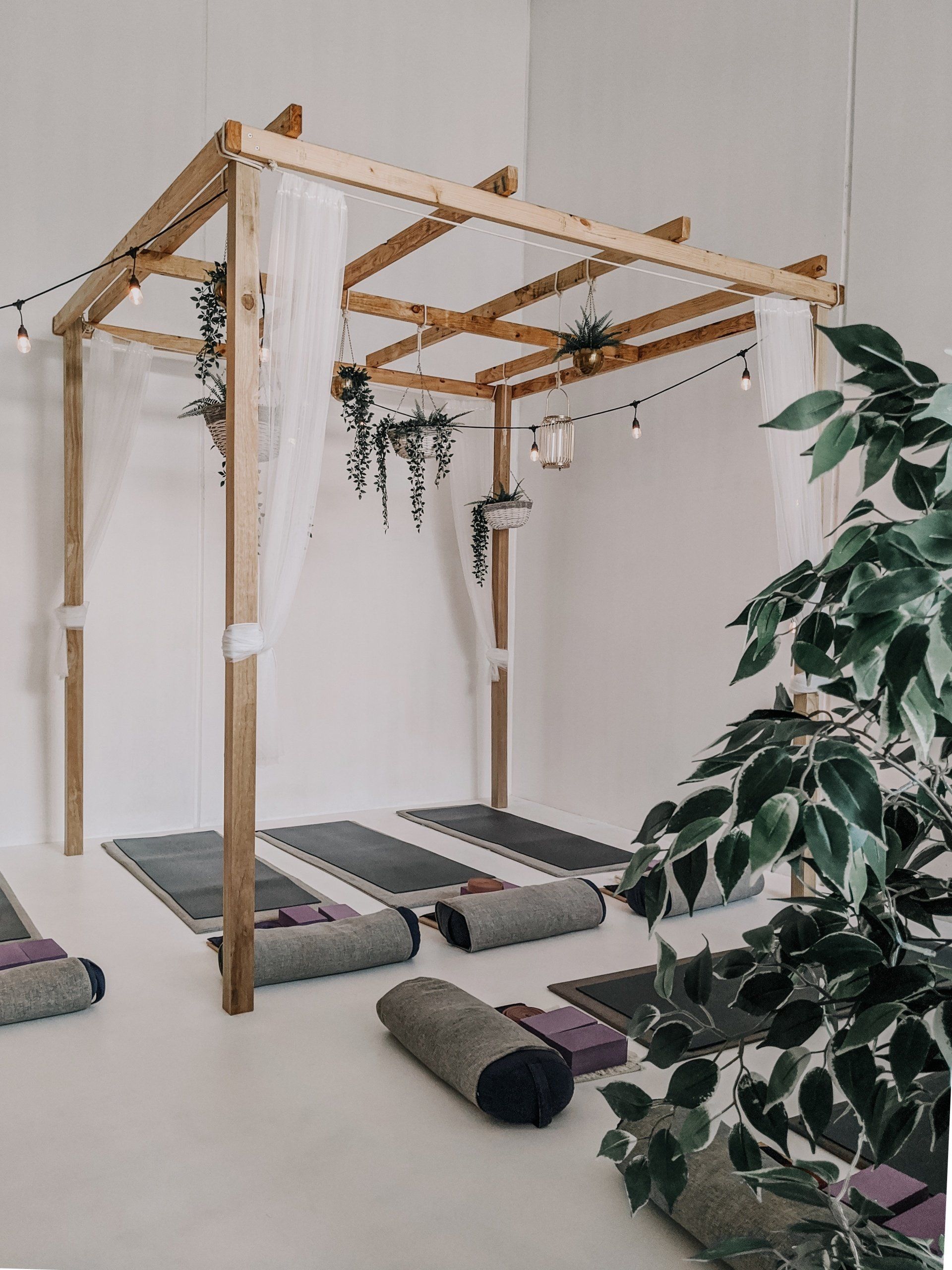 A room with yoga mats and pillows under a wooden canopy.