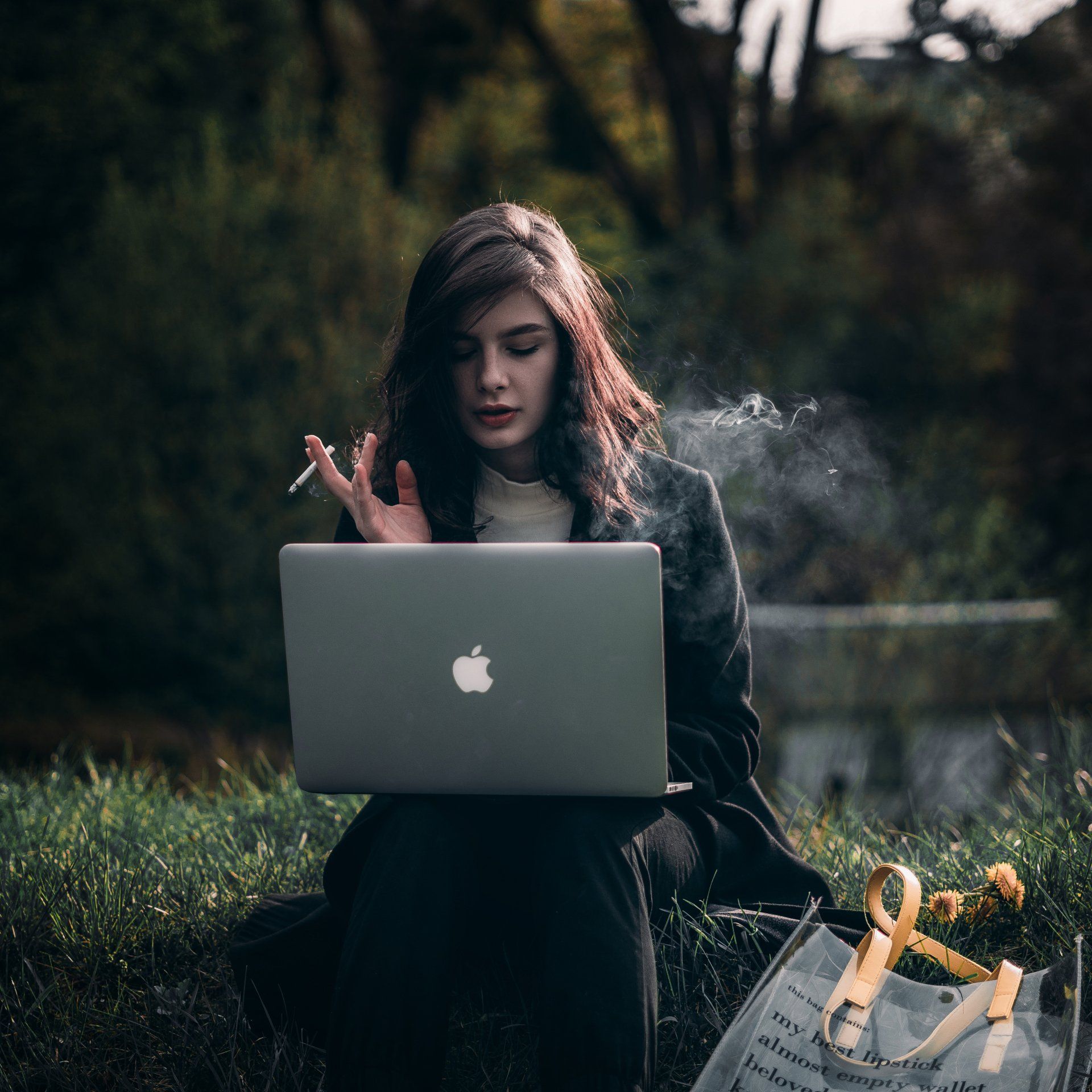 Woman sitting on a bench with a laptop, smoking a cigarette.