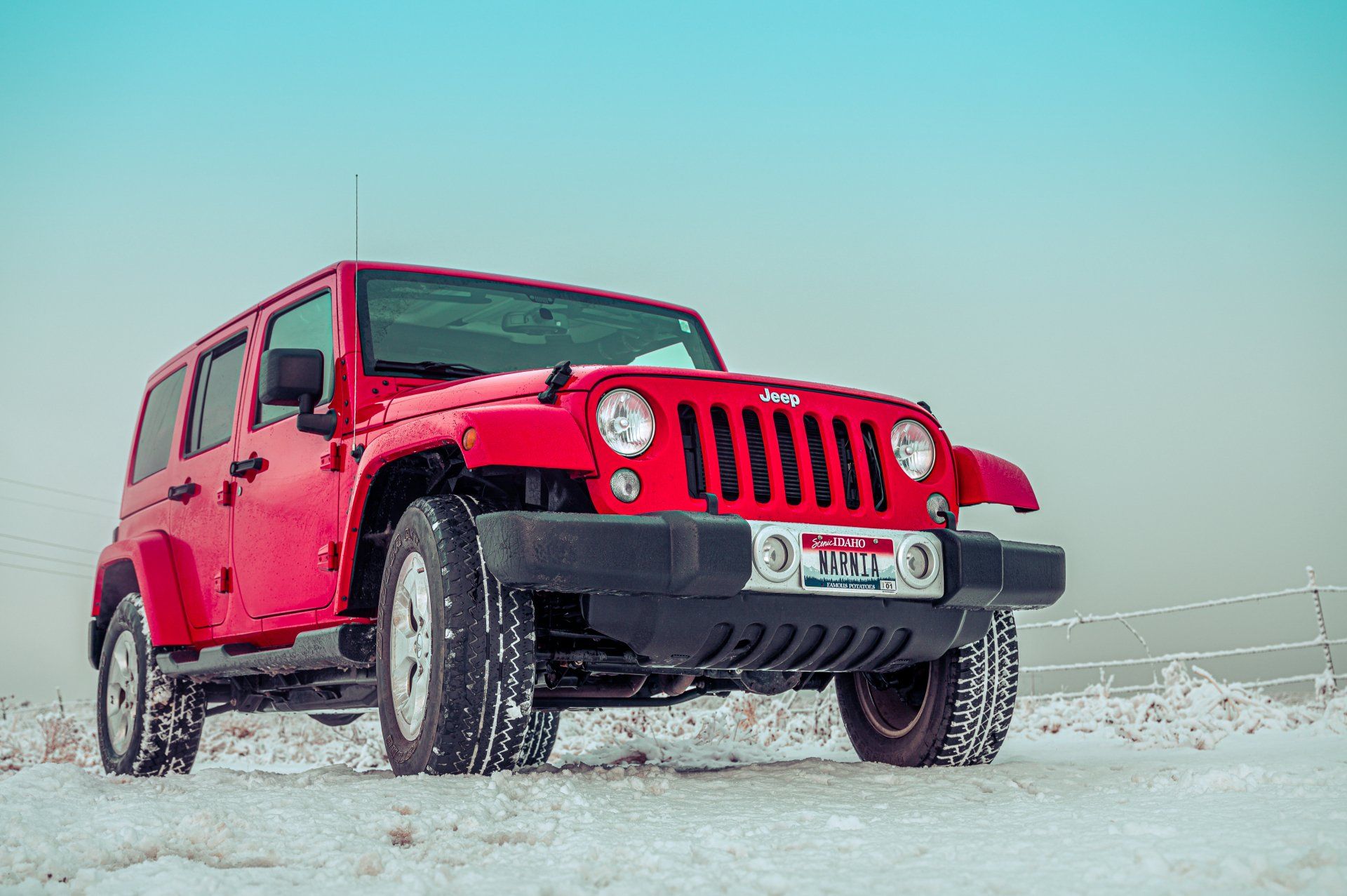A red jeep is parked in the snow in a field.