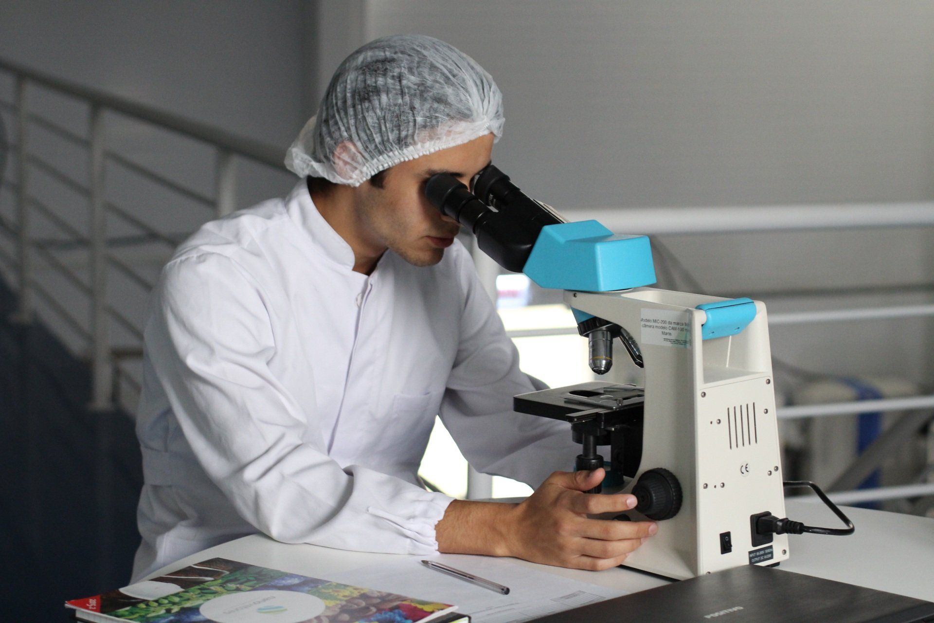 Man wearing white scrubs looking into microscope in a science lab.