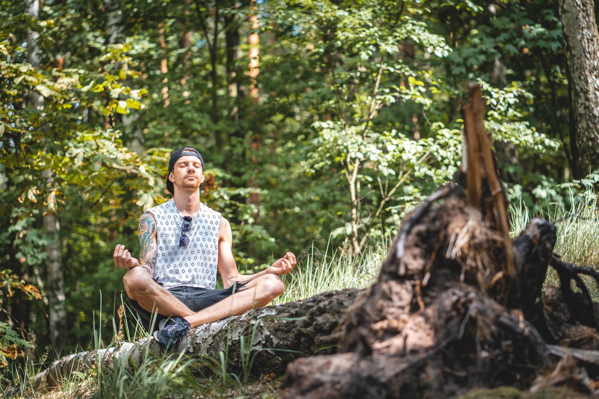 a man is sitting in a lotus position on a log in the woods.