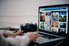 A person is typing on a laptop computer with a camera in the background.