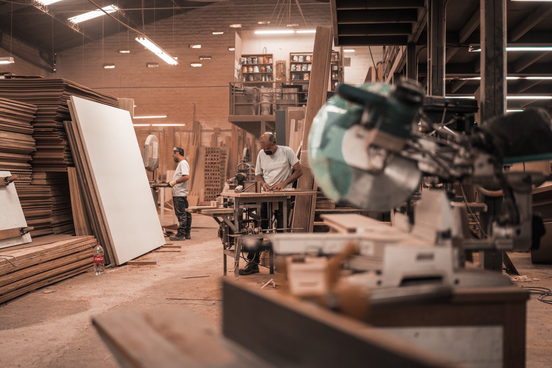 A skilled carpenter working diligently at a woodworking station, surrounded by neatly stacked plywood sheets and an array of essential woodworking tools and equipment.