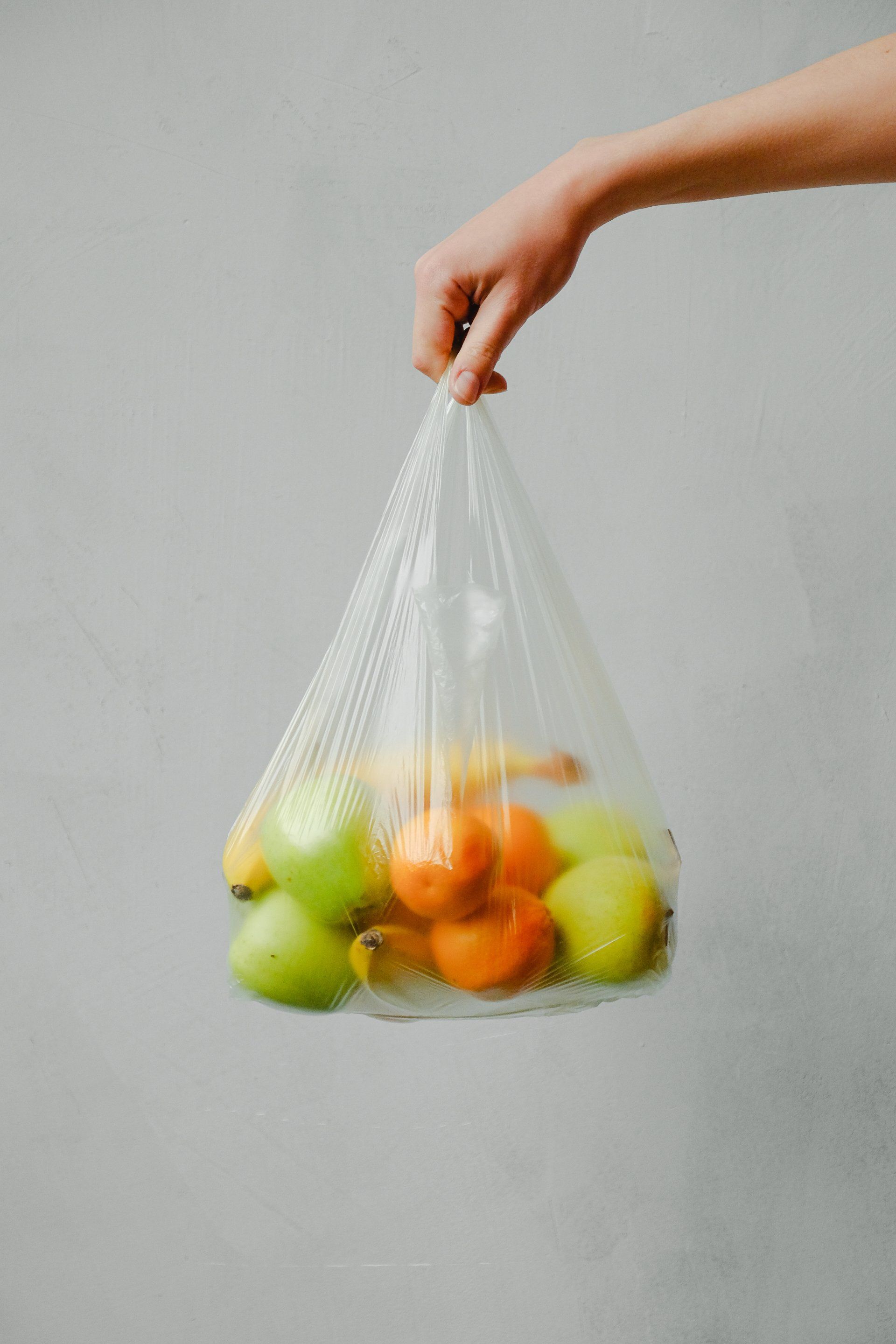 A person is holding a plastic bag filled with fruit.