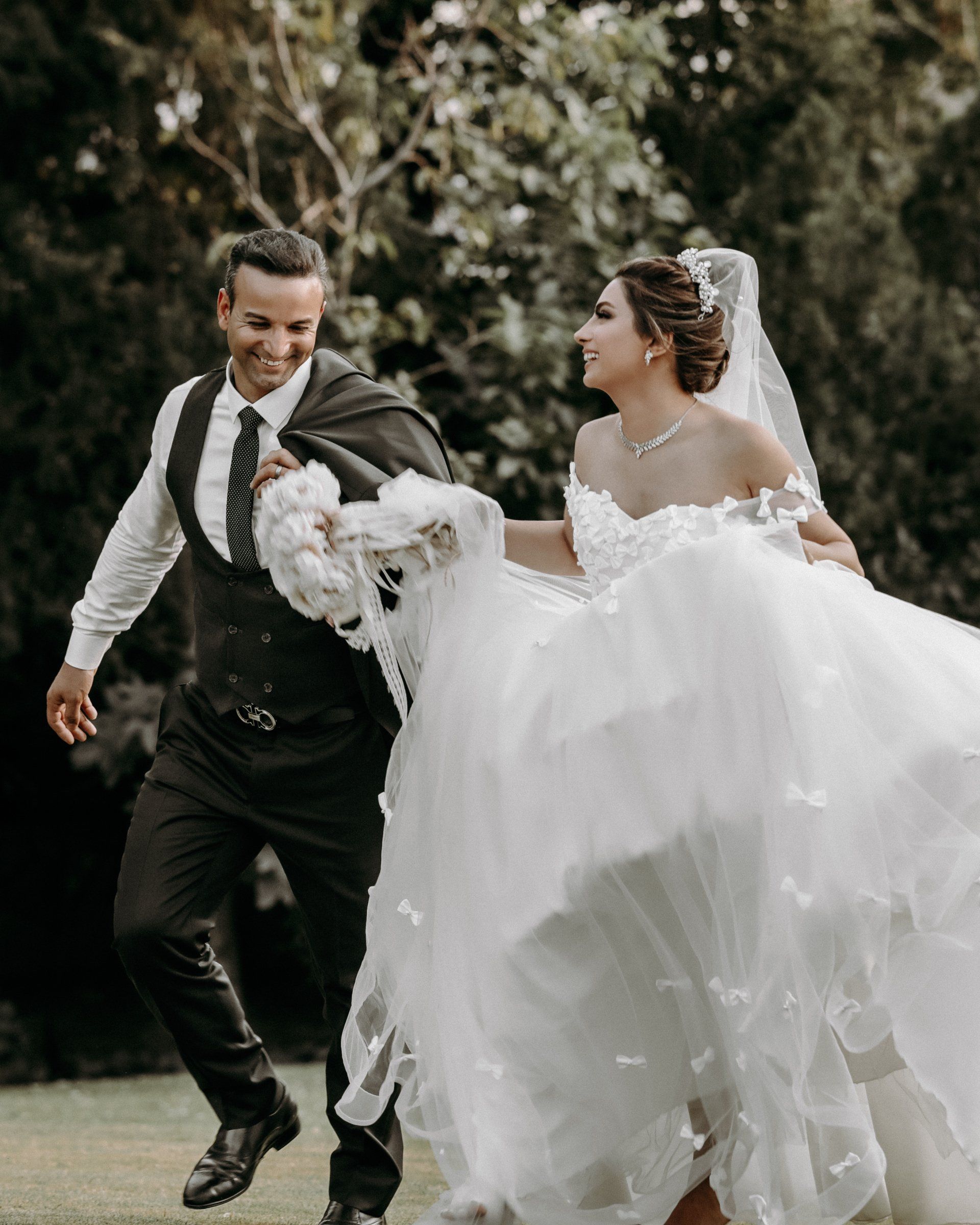 A bride and groom are running together in a park.