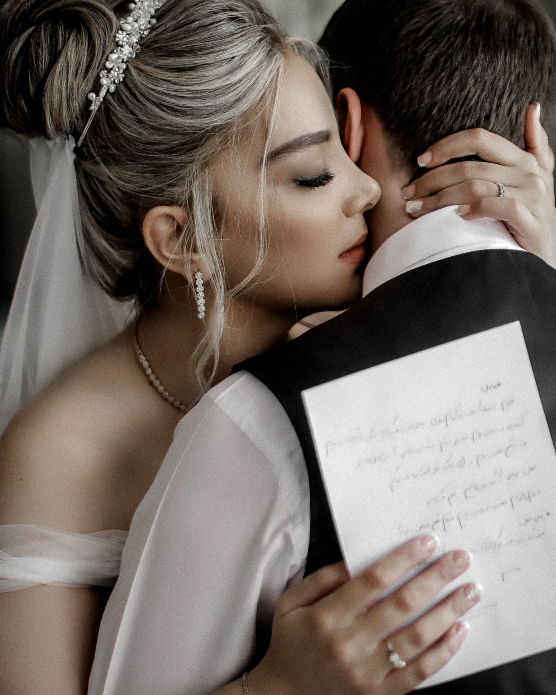 a bride is kissing the back of a groom while holding a premarital agreement .