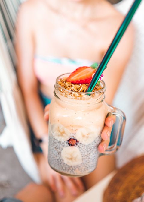A woman is holding a smoothie in a mason jar with a straw.