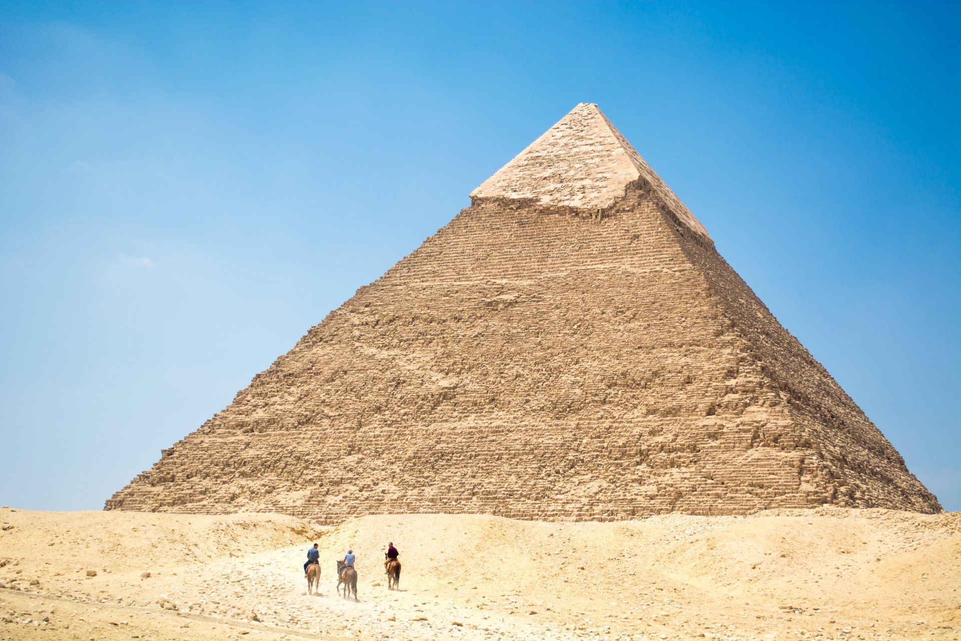 A group of people riding horses in front of a pyramid.