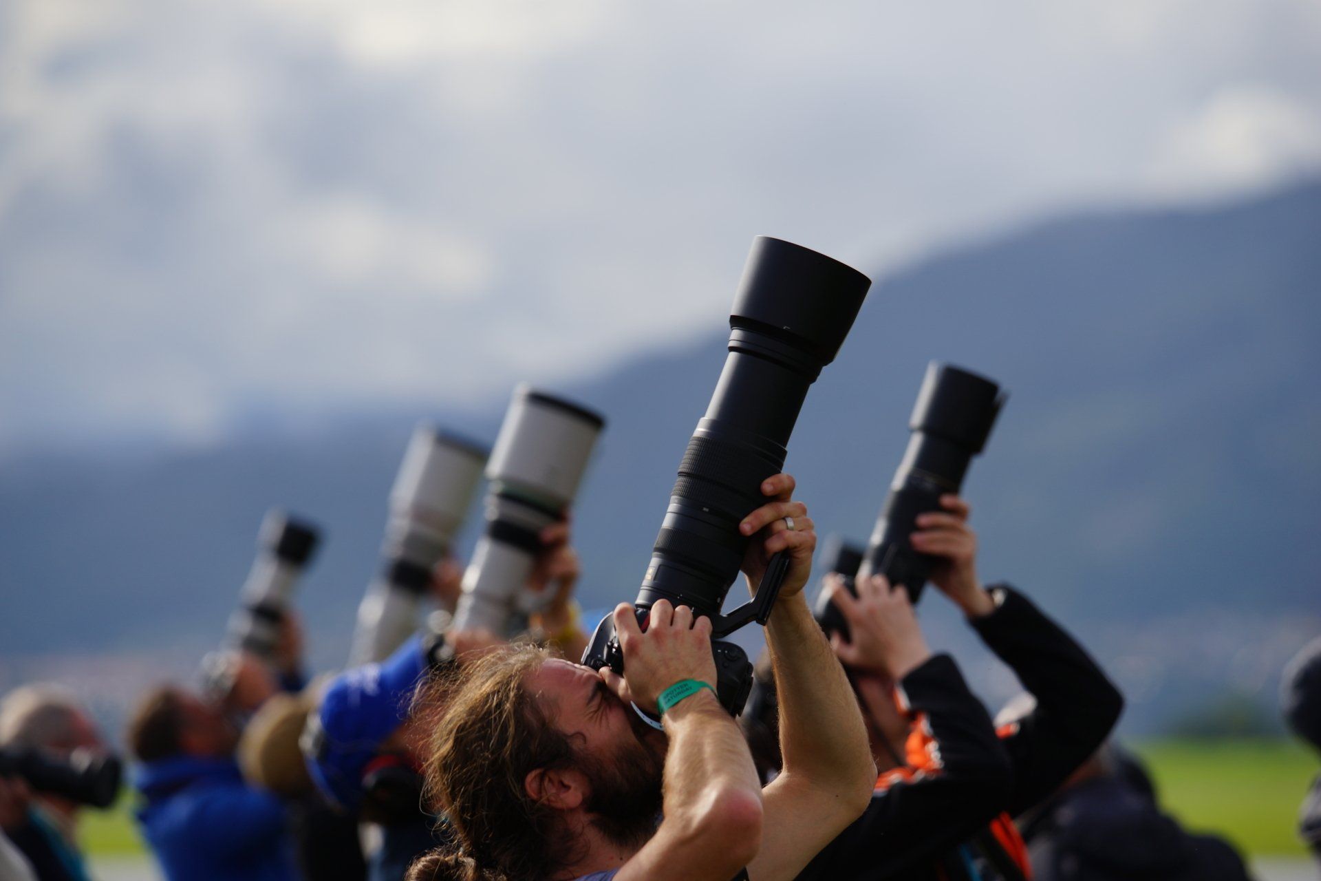 a man with a green wristband looks through a camera lens