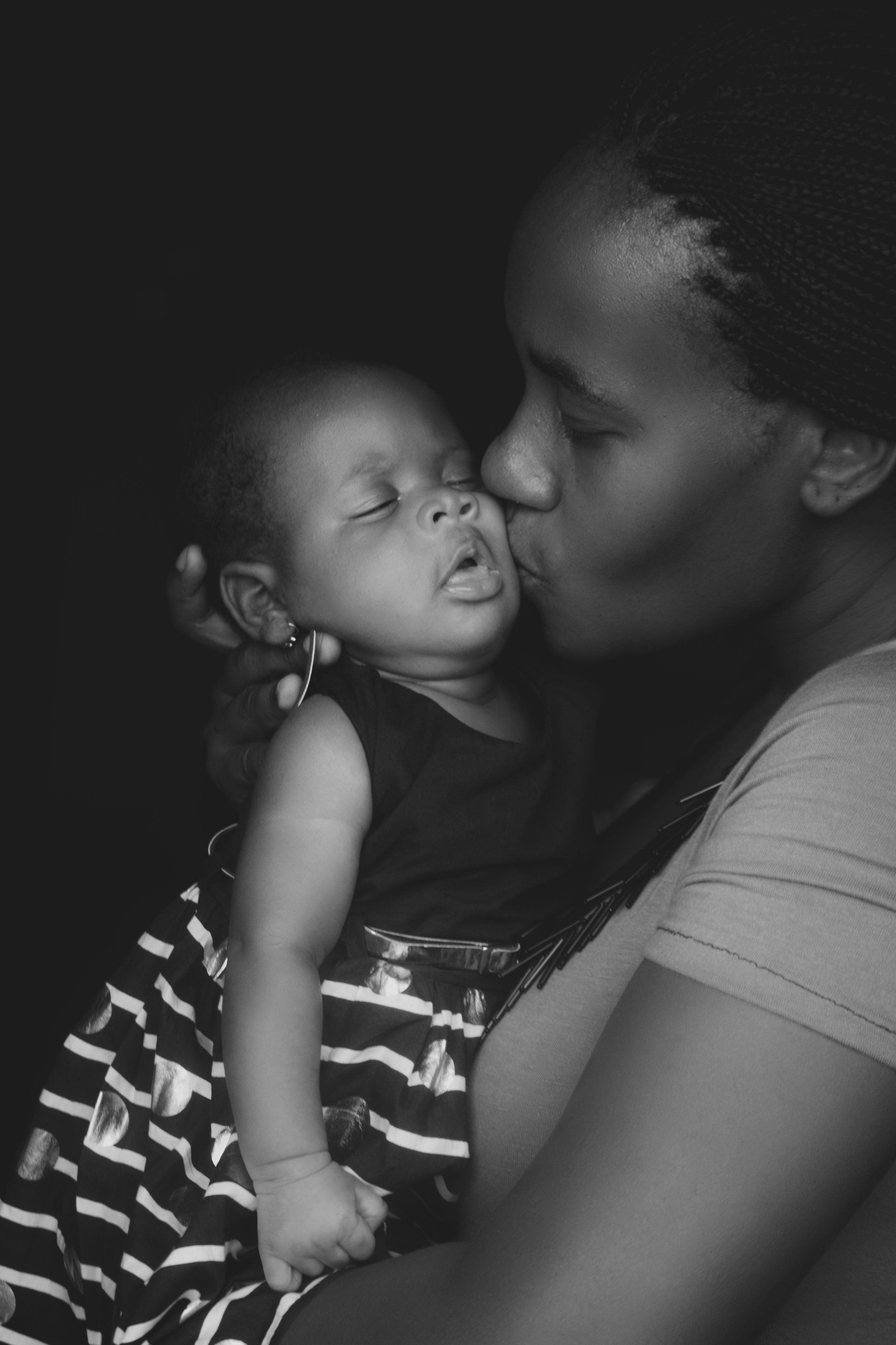 A woman is kissing her baby on the cheek in a black and white photo.