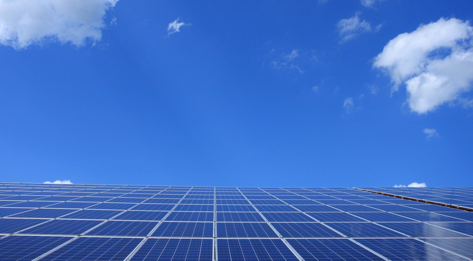 Solar panels below a blue sky with fluffy white clouds