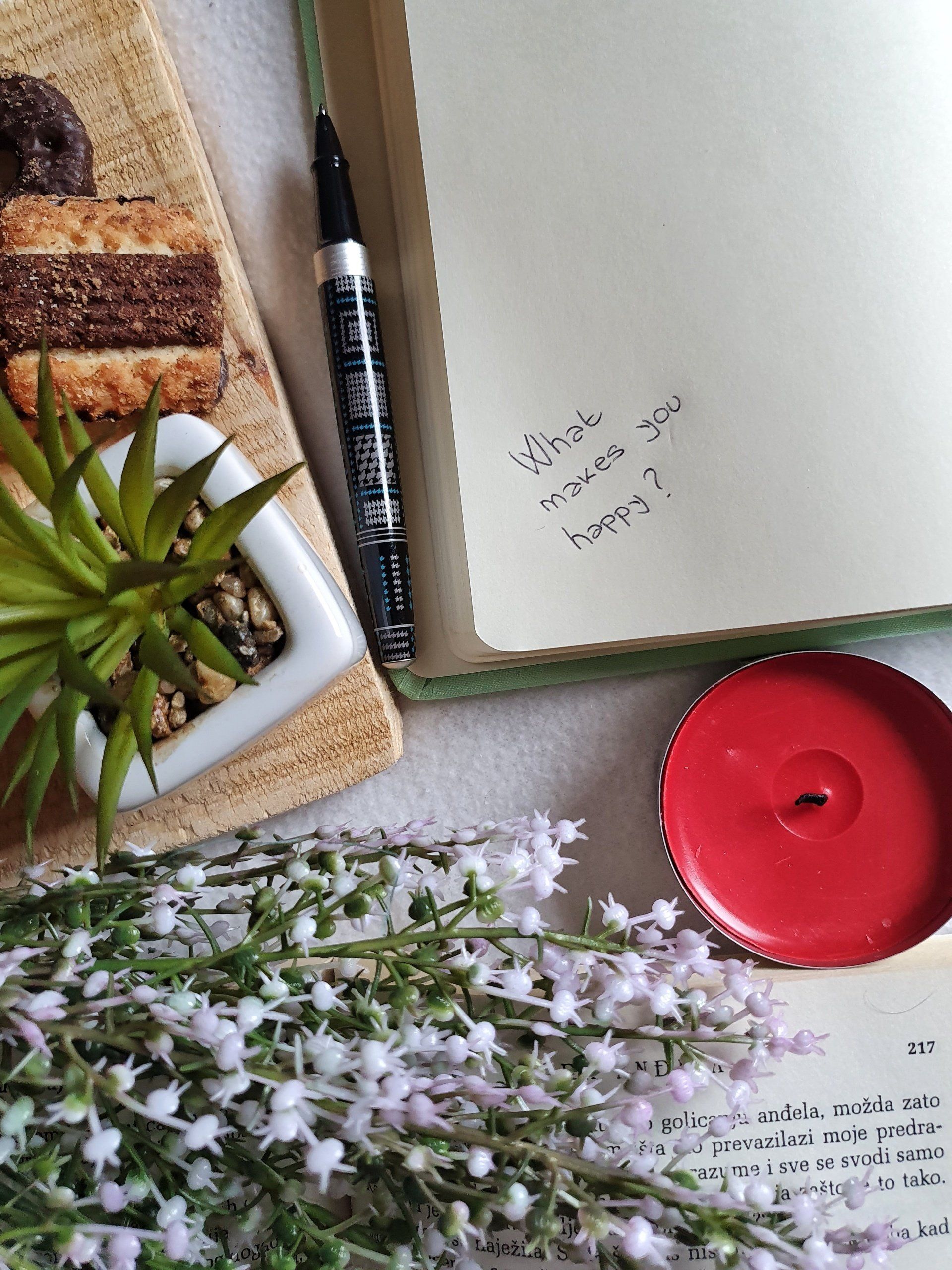 Notepad with writting saying what makes me happy on a table with candle, flower and a plant