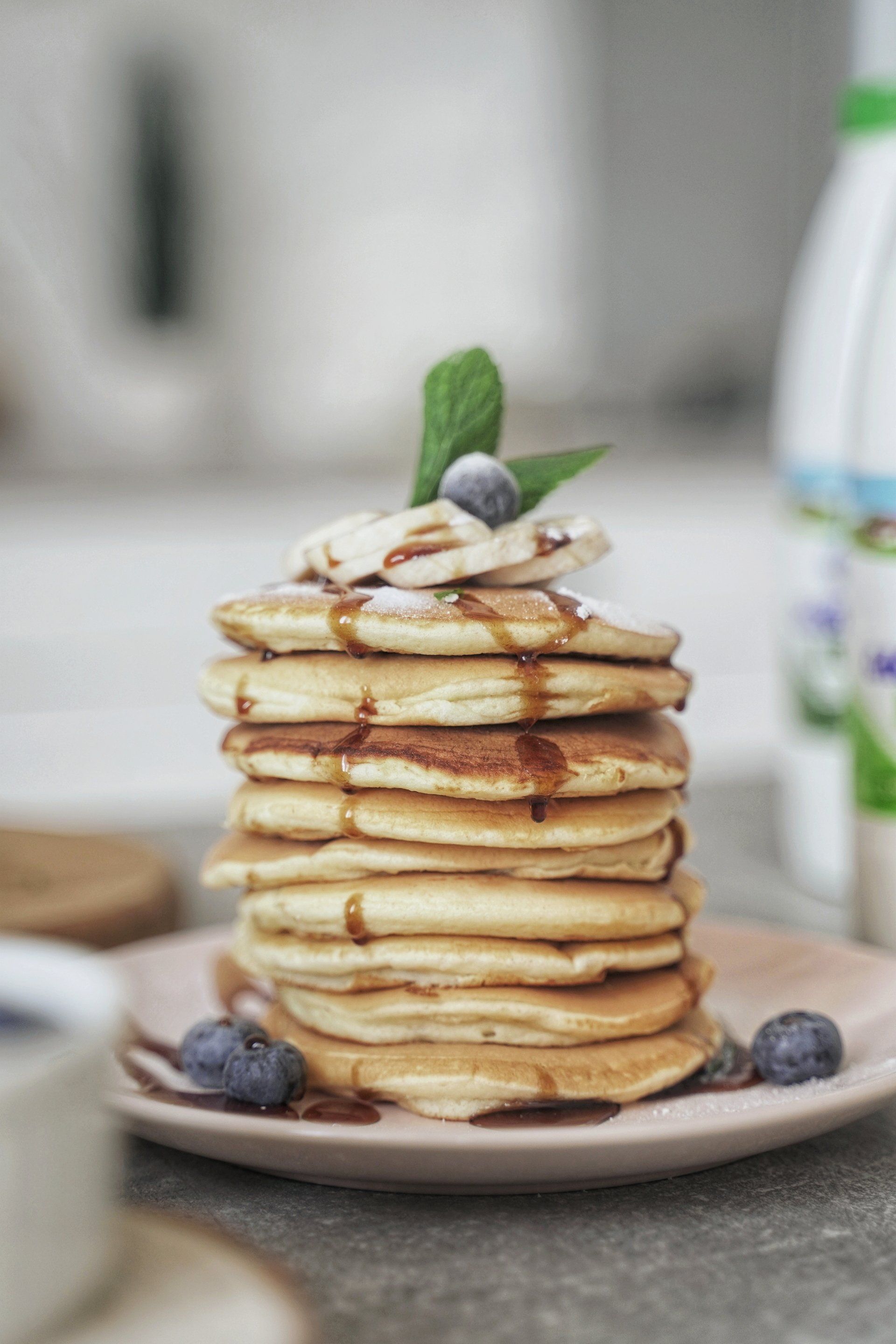 A stack of pancakes with blueberries and bananas on top on a plate.