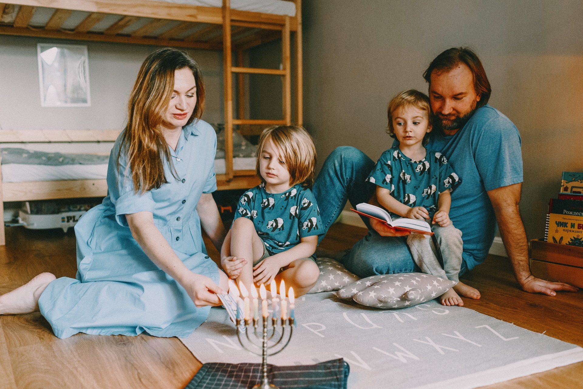 a family sits on the floor reading a book and lighting a menorah