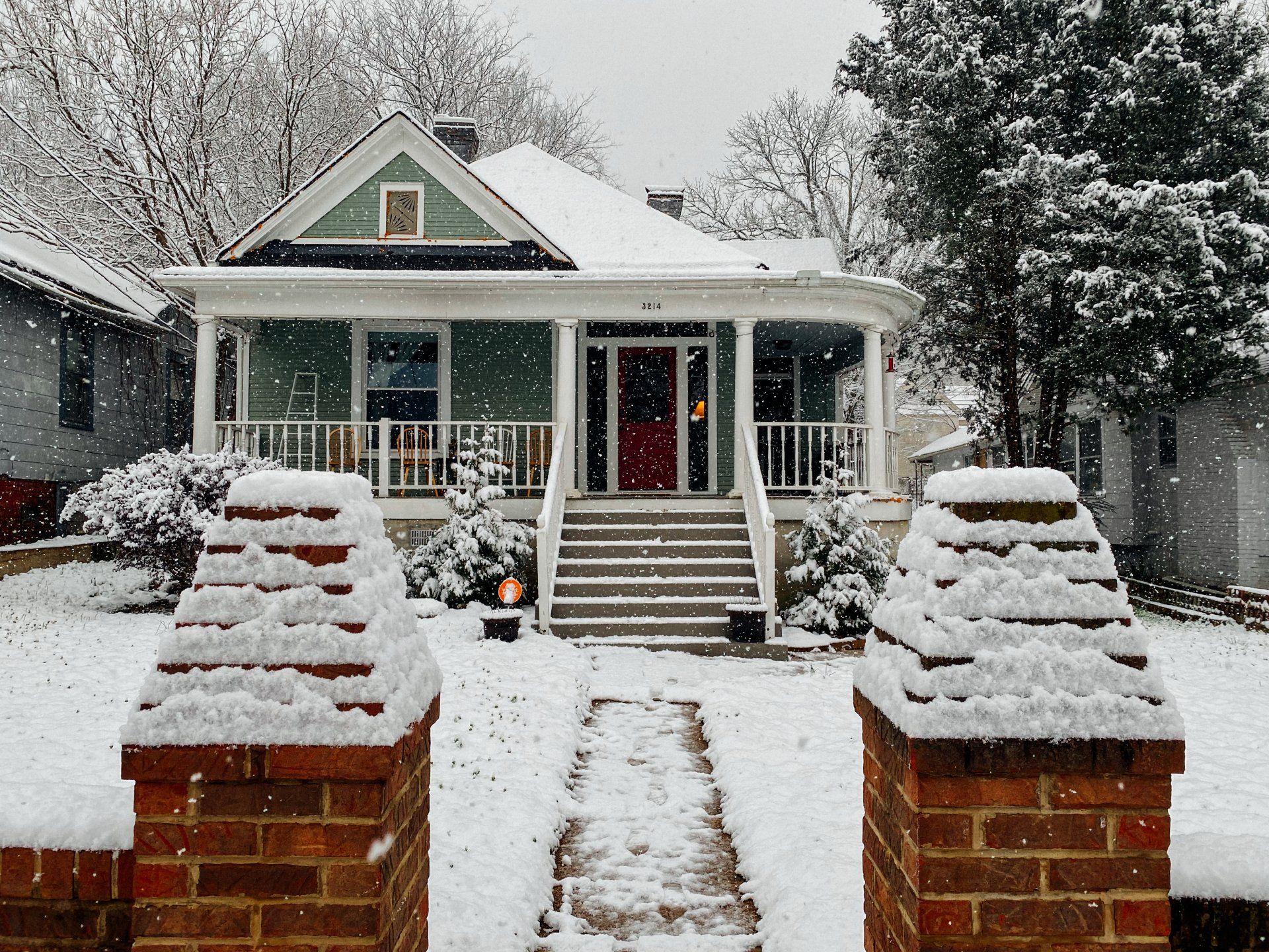 A partially-cleared walkway leads to a house as snow falls