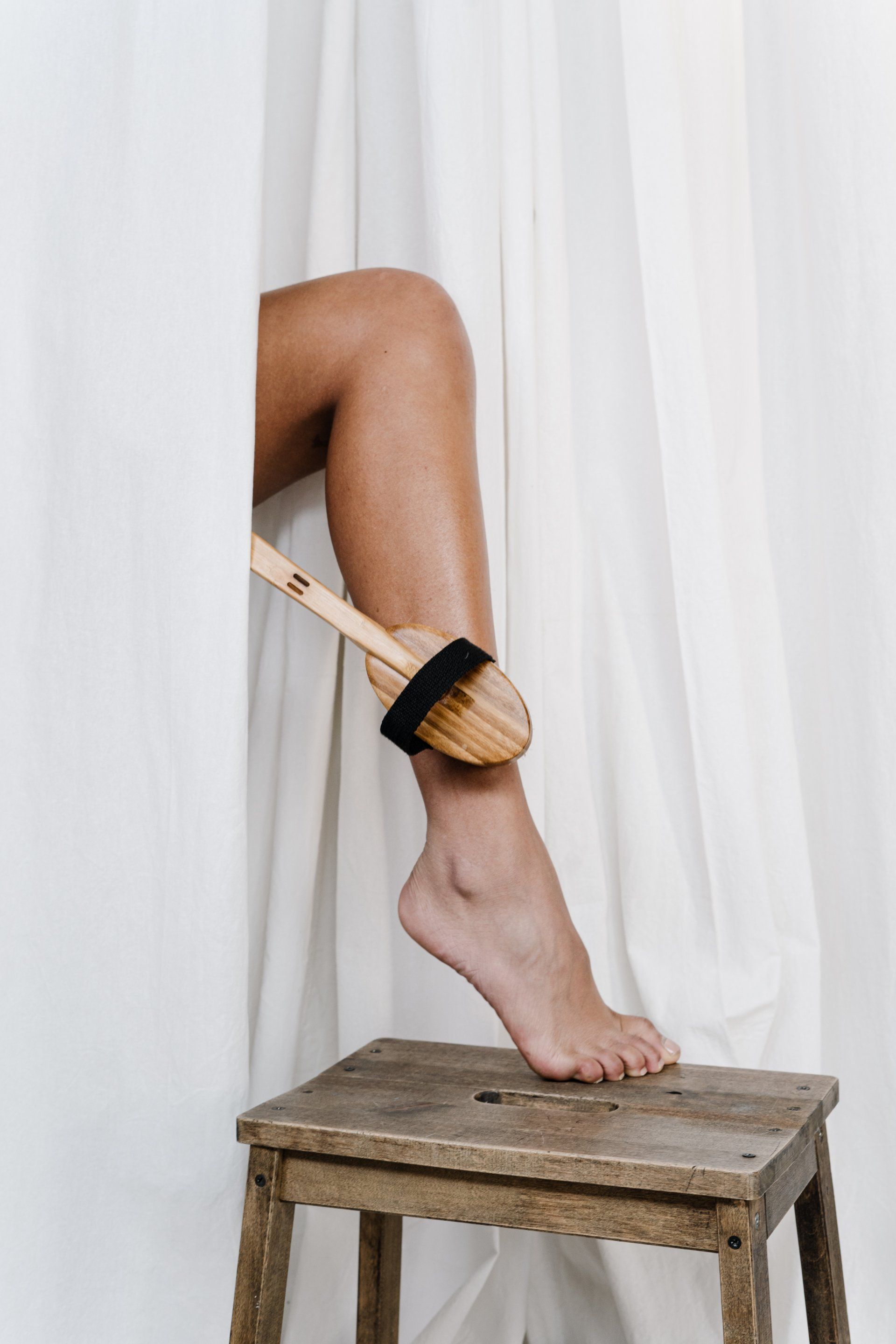 A woman is sitting on a wooden stool with a brush on her leg.