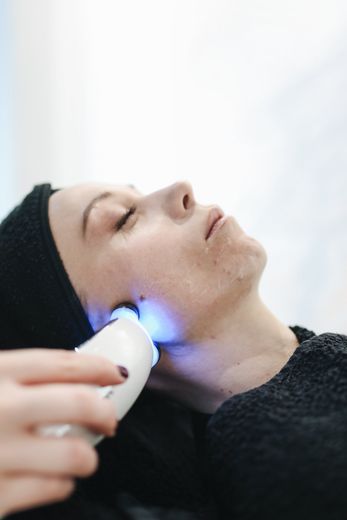 A woman is getting a blue light treatment on her face.